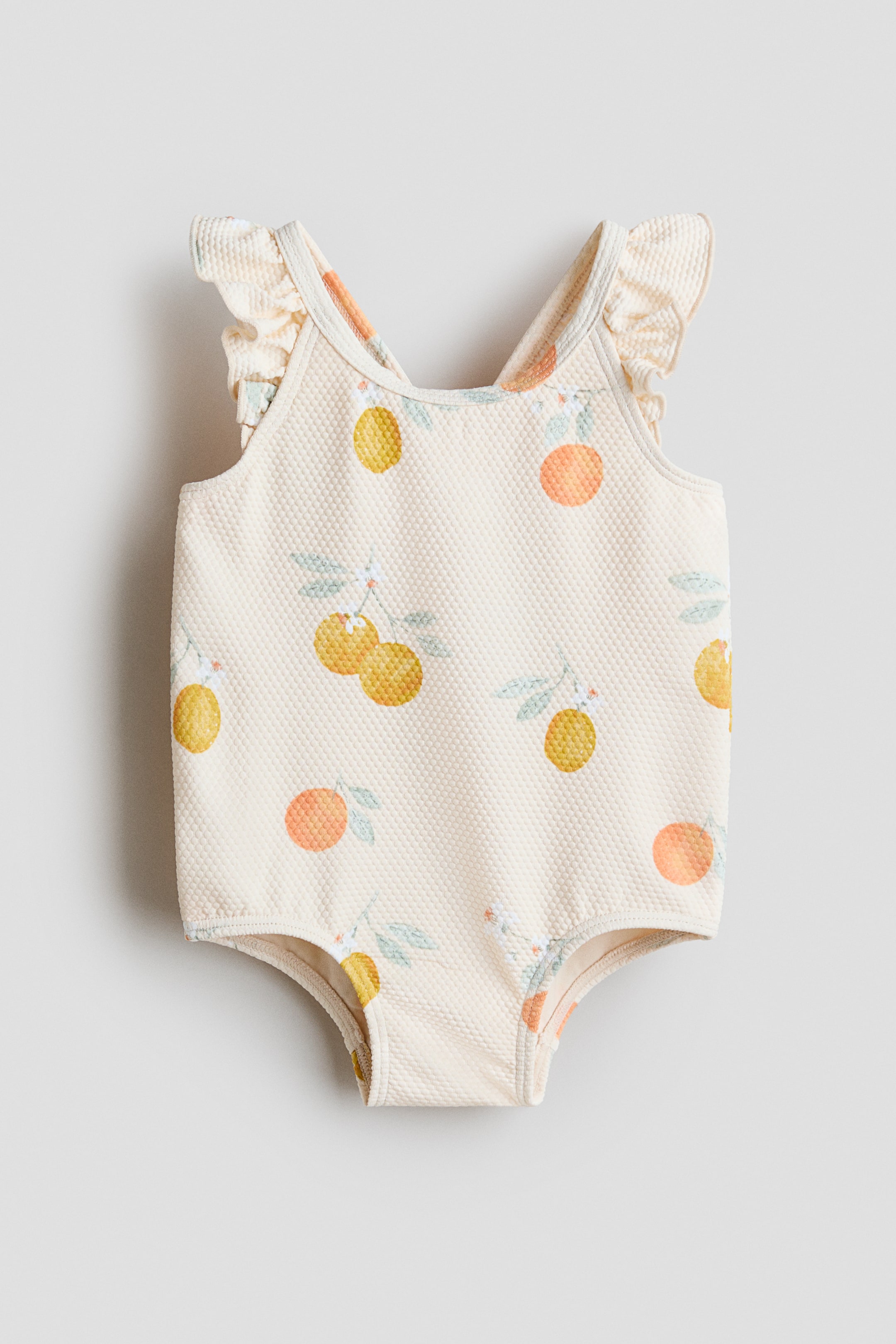 View larger image: This cream-colored swimsuit is showcased from the front, highlighting a waffle-knit texture and an all-over print of oranges, lemons, and leaves. It features a round neckline and frill-trimmed shoulder straps.