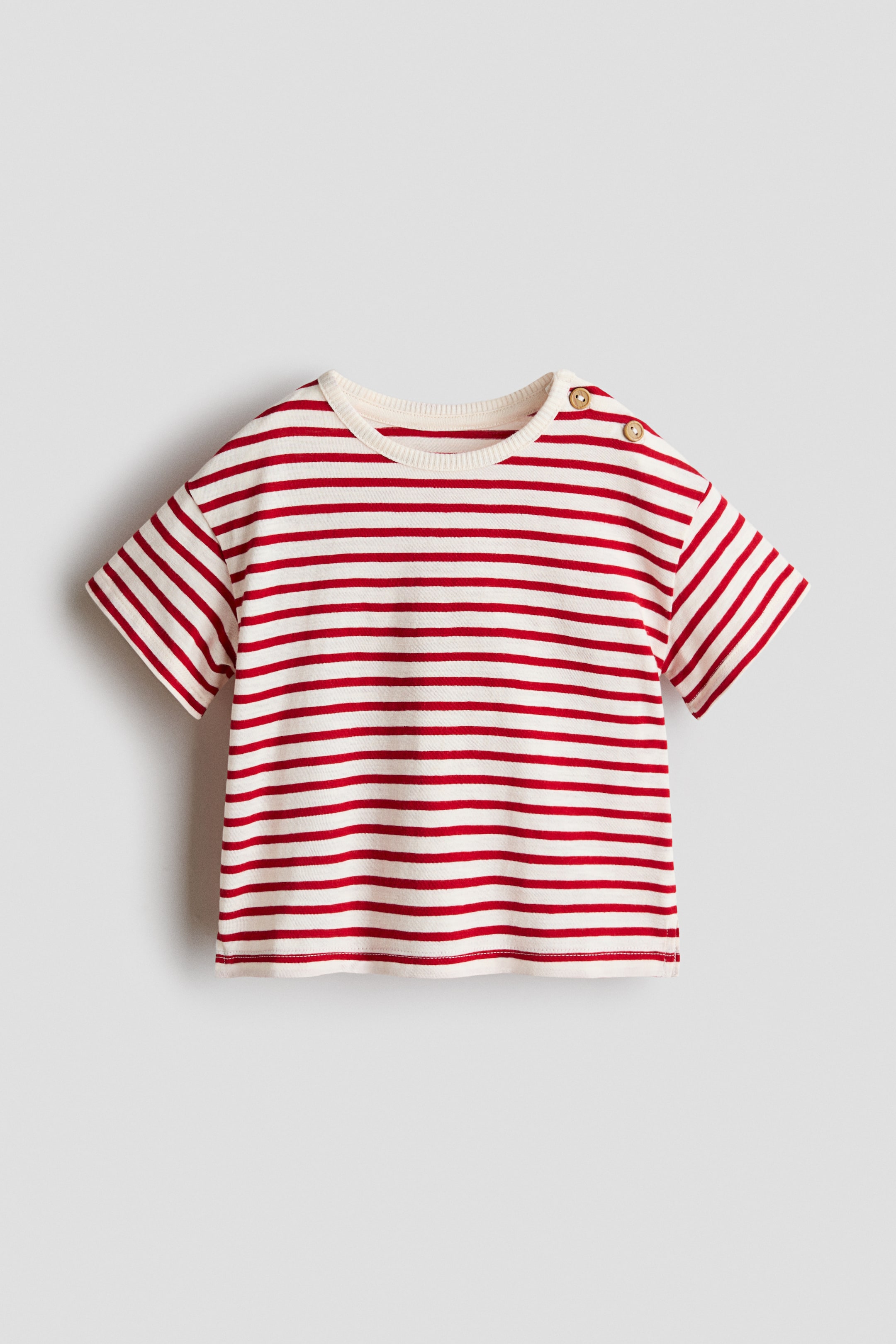 View larger image: A short-sleeved t-shirt is presented from the FRONT, lying flat, displaying red and off-white horizontal stripes, a ribbed round neck, and two wooden buttons on the left shoulder.