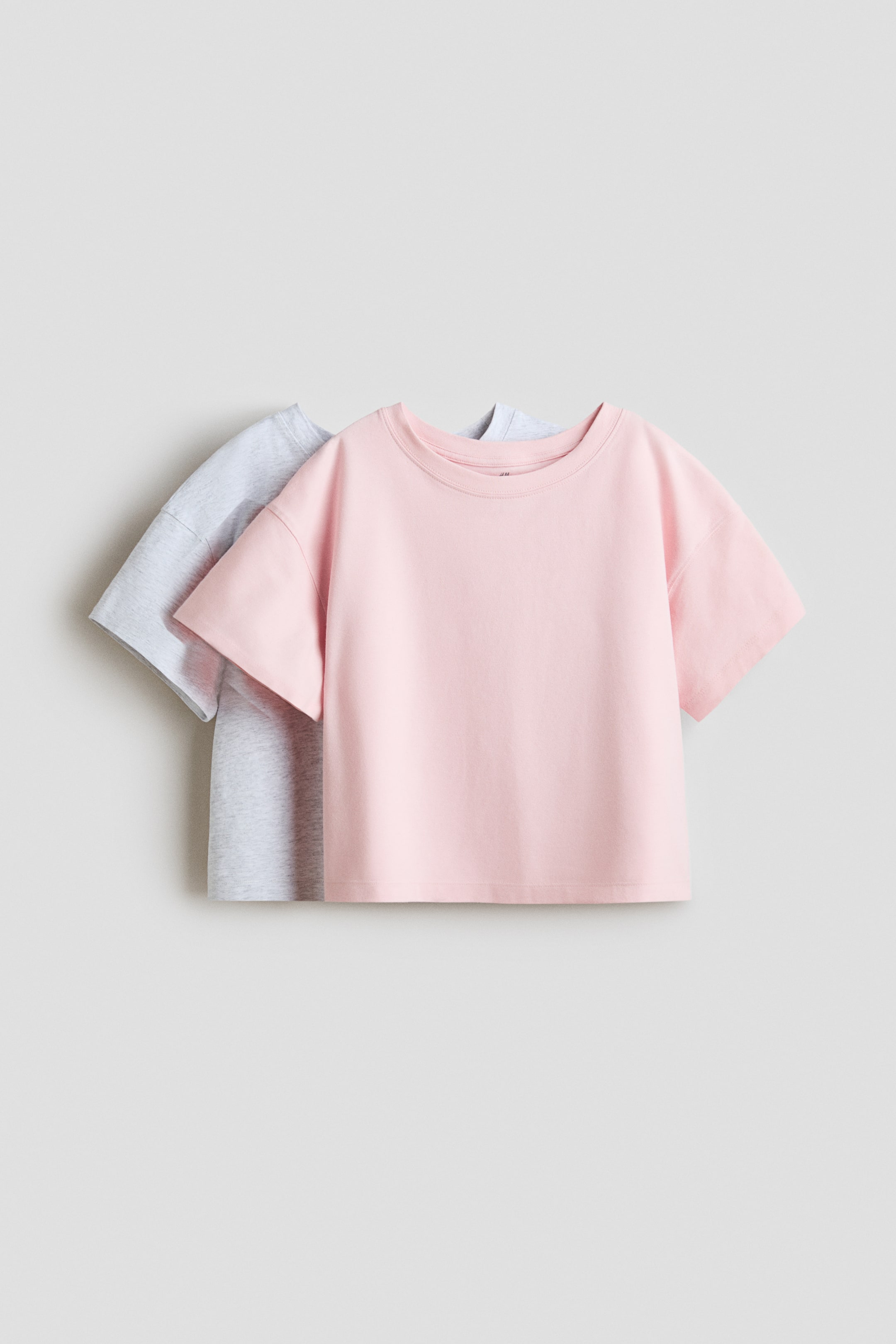 Agrandir l'image: Deux t-shirts en jersey de coton doux présentent leurs vues de face, avec un t-shirt rose superposé devant un t-shirt gris clair. Les deux arborent un col rond, des épaules tombantes et des manches courtes.