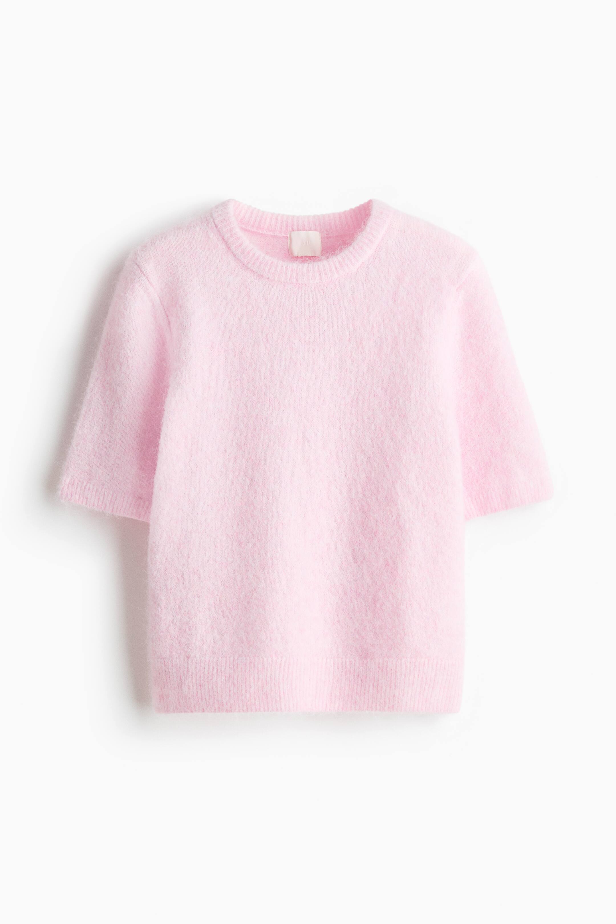 View larger image: A pink fluffy sweater is laid flat, showcasing a crew neck, short sleeves with ribbed cuffs, and a ribbed hem. A light-coloured tag is visible at the back of the neck.