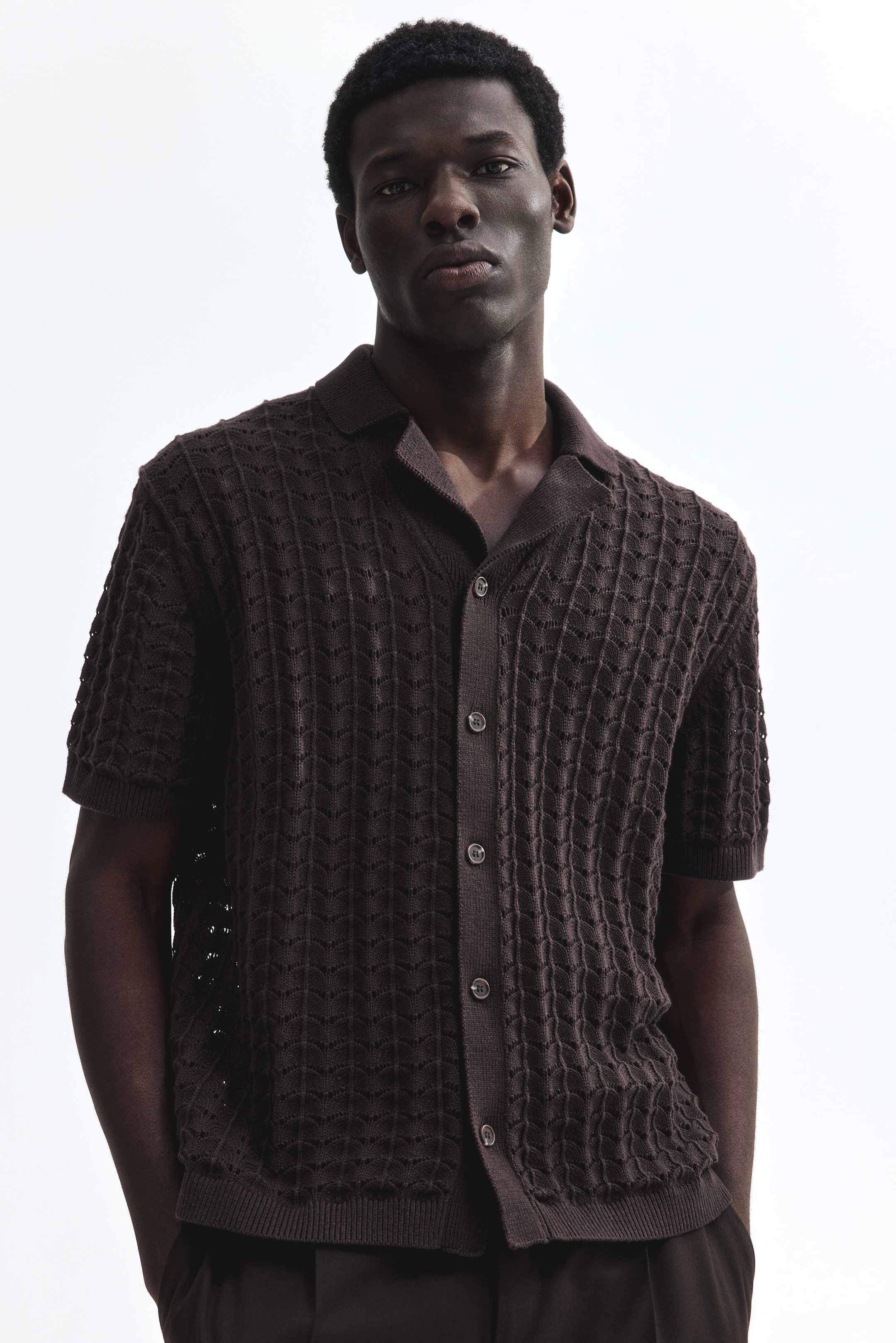 View larger image: The model is wearing a dark brown short-sleeved pointelle knit shirt. It boasts a resort collar, buttons down the front, a straight hem, and a relaxed fit.