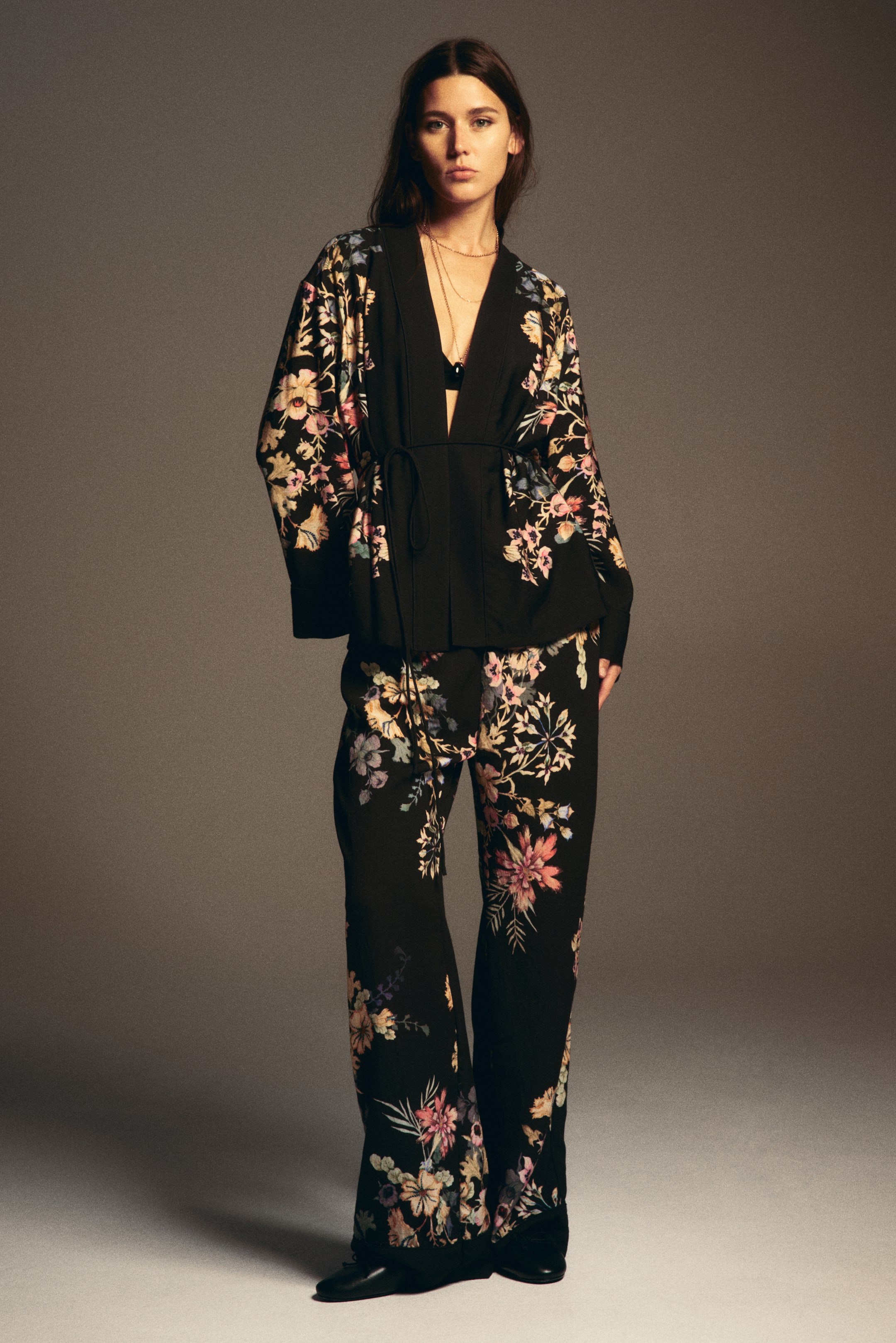 View larger image: A black floral matching set is featuring a kimono-style top with wide sleeves and a tie-waist, paired with wide-leg trousers, both displaying a vibrant floral pattern in pink, blue, and yellow tones.