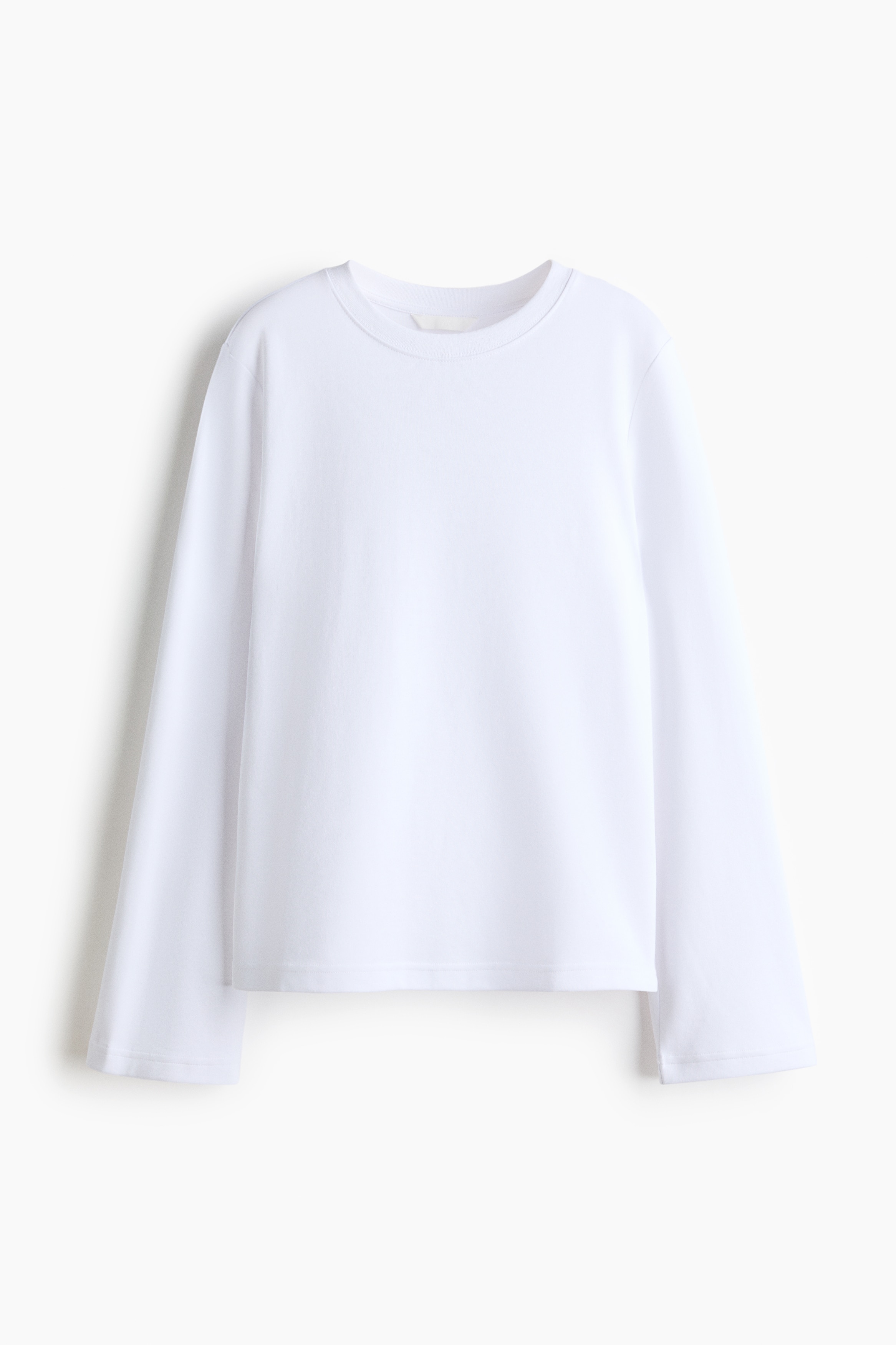 The model is wearing a white loose-fit top in heavy interlock jersey, featuring a round neckline with rib trim, dropped shoulders, and long sleeves. The top is styled with light grey wide-leg trousers.