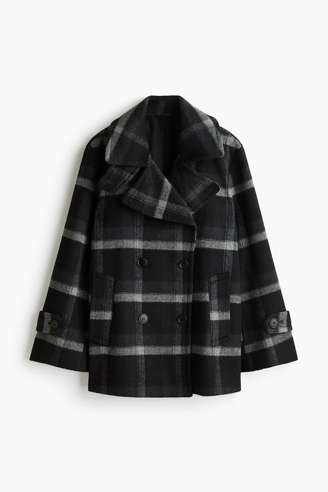 A double-breasted pea coat in a black and grey plaid pattern is shown facing front, featuring wide notch lapels and a double-breasted button closure. The design includes vertical welt pockets and button-tab details on the cuffs. - 1