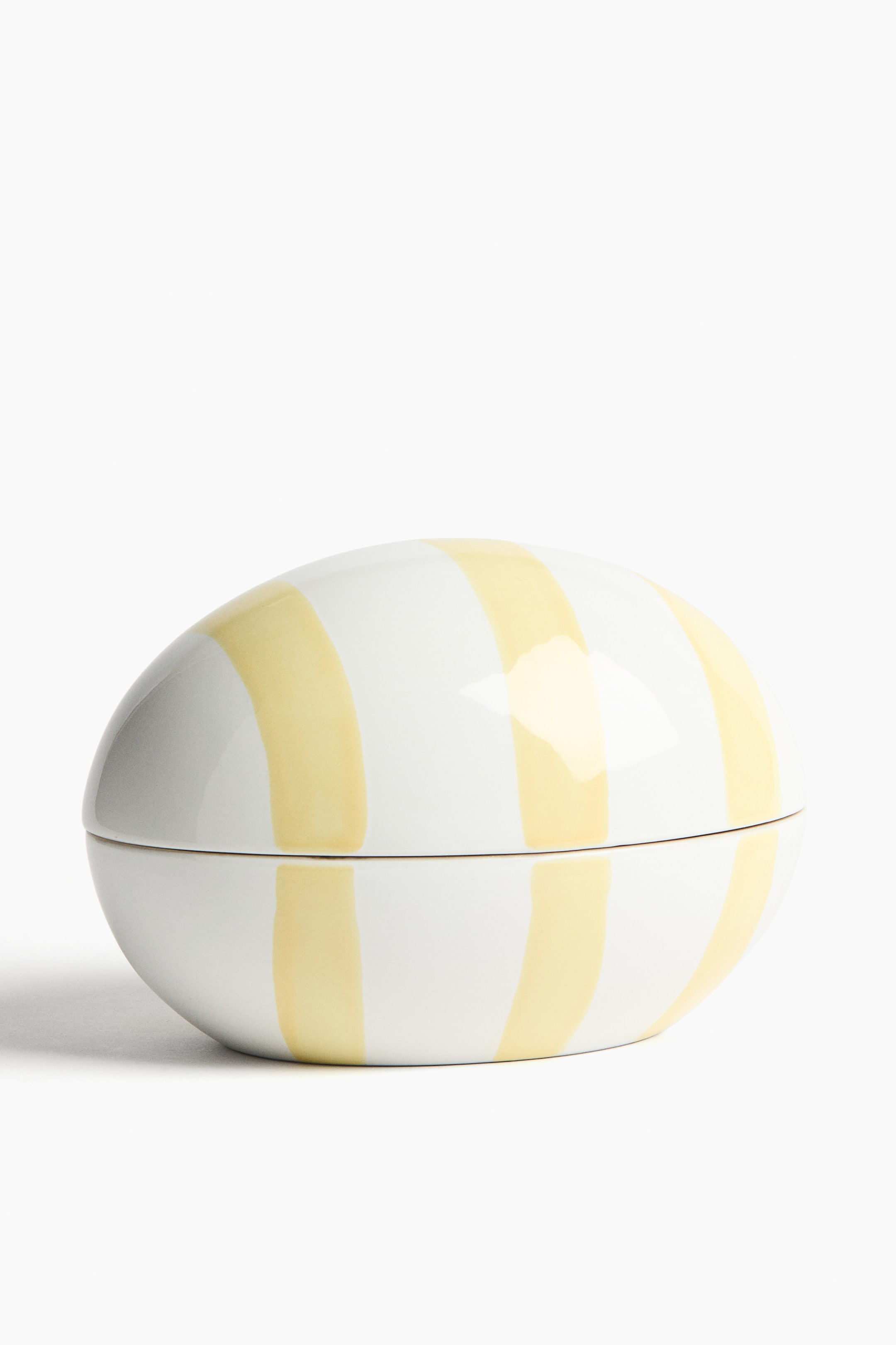 View larger image: An egg-shaped container faces forward, revealing a white surface with irregular vertical yellow stripes. The container consists of a top lid and a bottom base that meet along a horizontal seam.