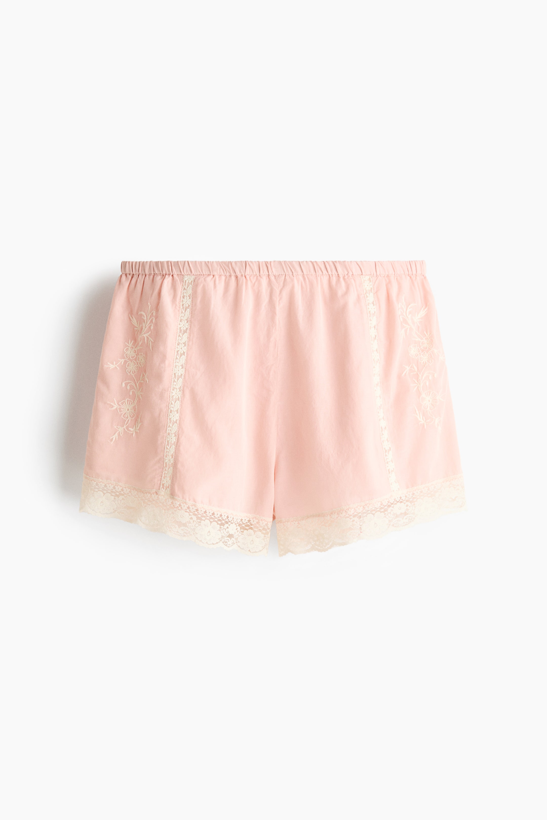 View larger image: "Pink shorts are showcased from the front, featuring an elasticised waistband. White floral embroidery embellishes the outer side panels, while vertical white lace inserts adorn the front. A wide white lace trim finishes the leg openings."