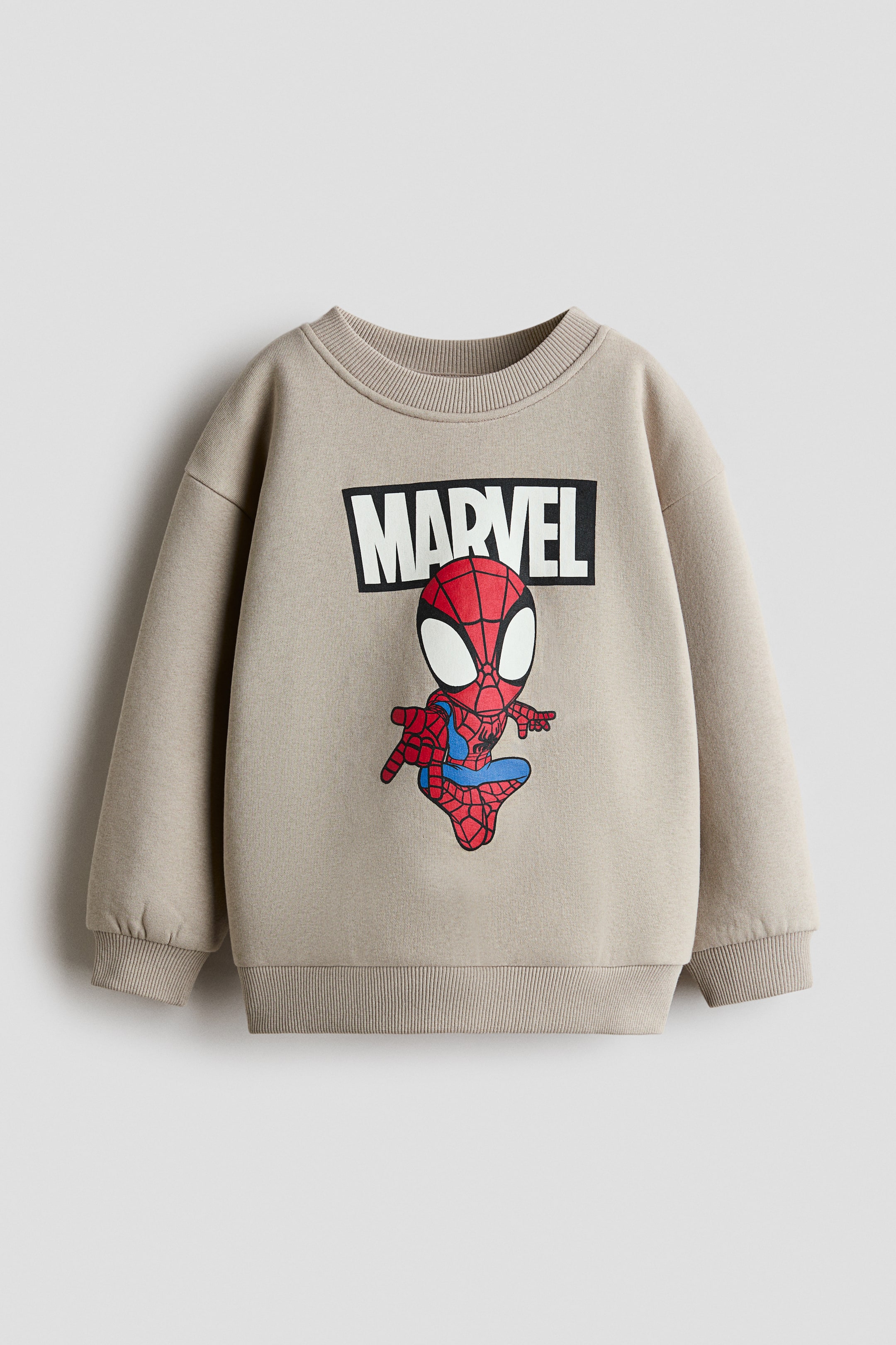 Ver imagen más grande: Se muestra una sudadera beige desde el frente, con un gráfico impreso de la palabra "MARVEL" en letras blancas de estilo bloque dentro de una caja rectangular negra, encima de una ilustración de Spider-Man tipo dibujo animado. La prenda presenta cuello redondo acanalado, hombros caídos y mangas largas con puños acanalados y bajo acanalado a juego.
