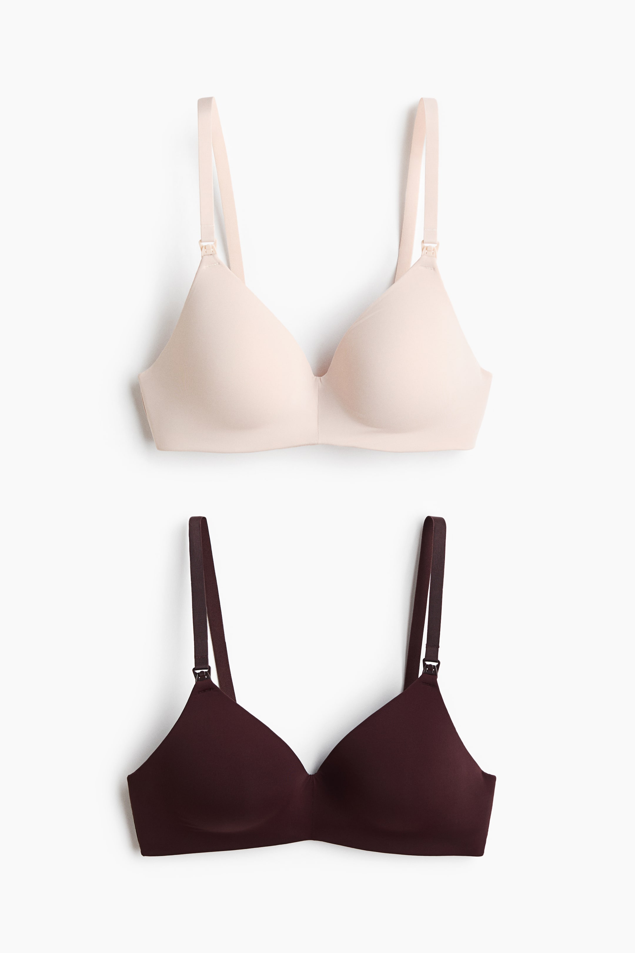 Größeres Bild ansehen: Zwei kabellose Still-BHs sind von vorne zu sehen, einer in hellem Beige und einer in dunklem Burgunderrot. Beide BHs verfügen über glatte, geformte Cups, verstellbare Schulterträger und kleine Stillverschlüsse am Ansatz der Träger.
