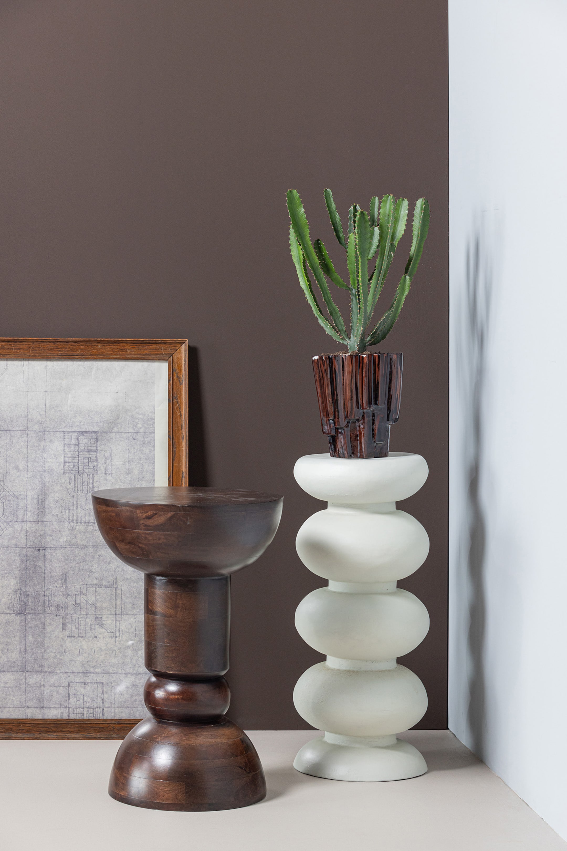 Agrandir l'image: Un piédestal blanc se tient droit, arborant une forme d'heureglass empilée et arrondie. Une plante cactus verte dans un pot sombre et texturé repose sur sa surface supérieure plate.