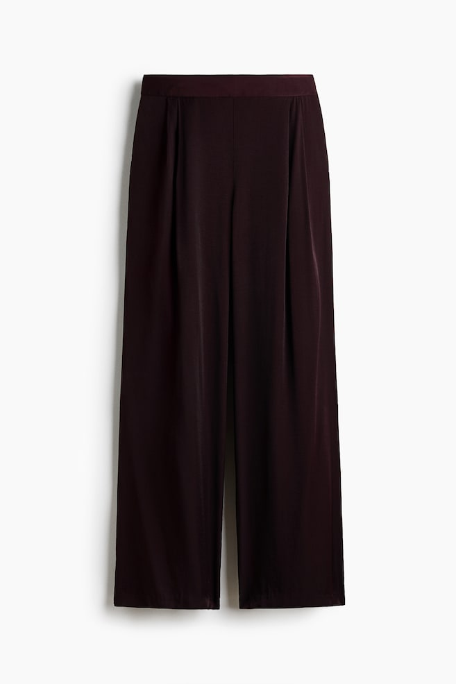 Pantalones de pierna ancha en color ciruela profundo con cinturilla plana y pliegues delanteros, que presentan un tejido suave y fluido. - 1