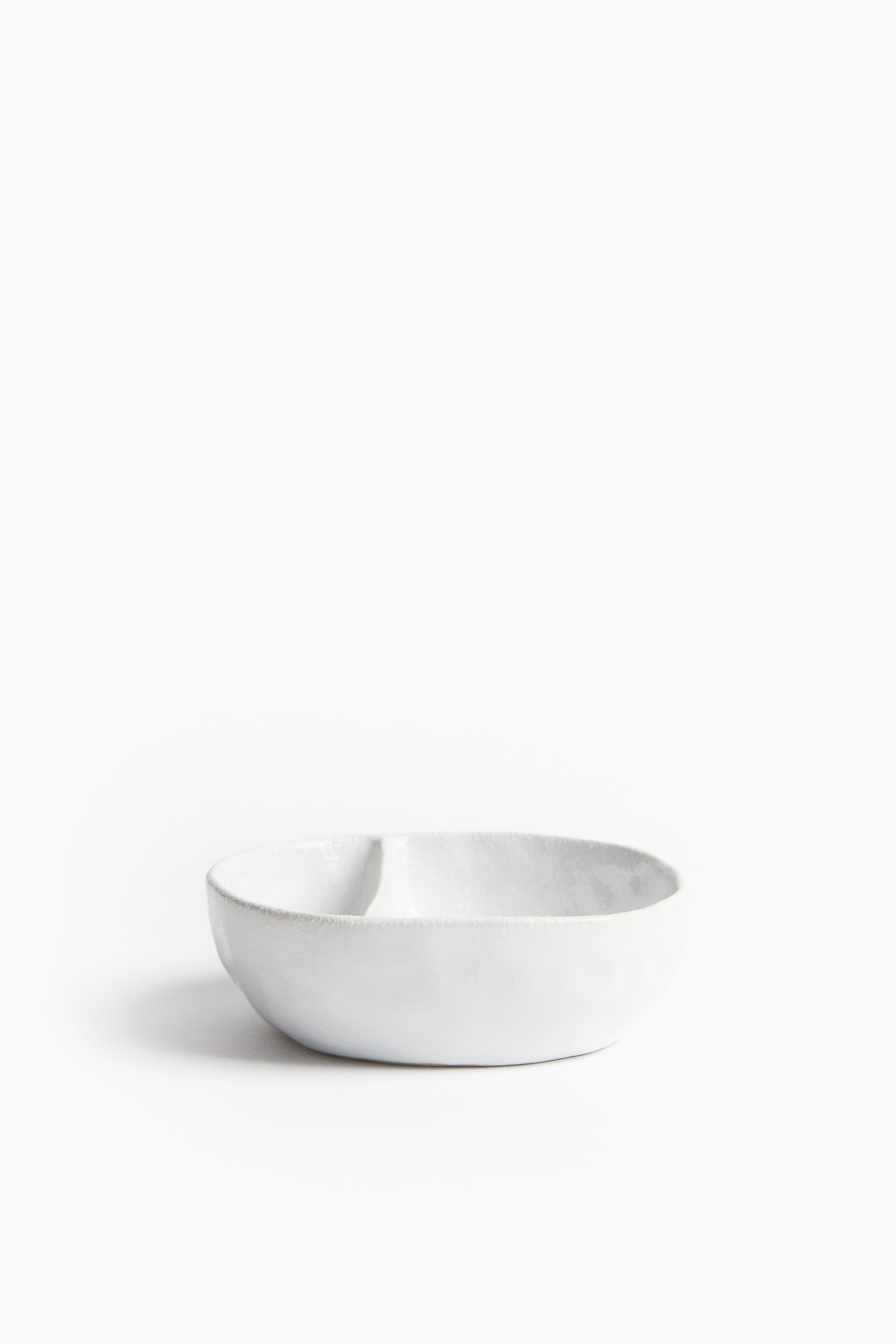 View larger image: A white ceramic bowl faces forward, showcasing two compartments divided by a central separator. The bowl displays a subtle, irregular texture on its surface and rim.
