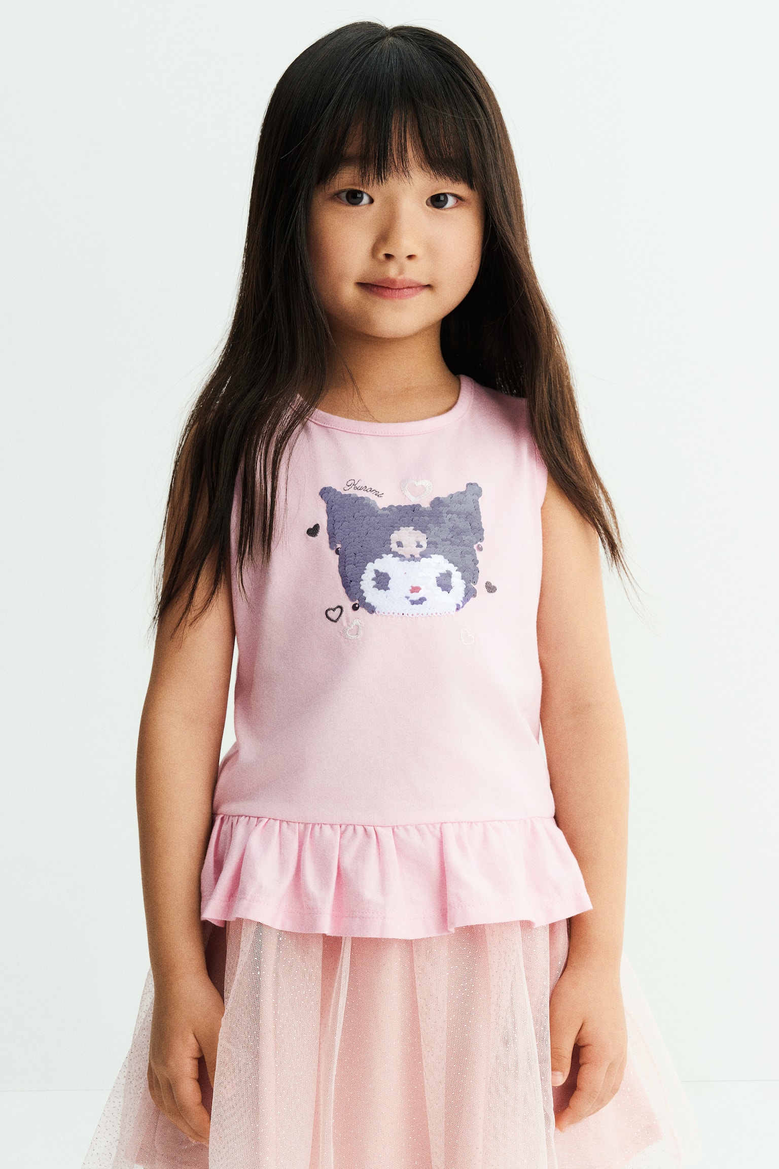 A light pink sleeveless top featuring a round neckline and a sequined character design on the front is worn by the model. The top has a flared frill trim at the hem and is styled with a matching pink tulle skirt. - 1