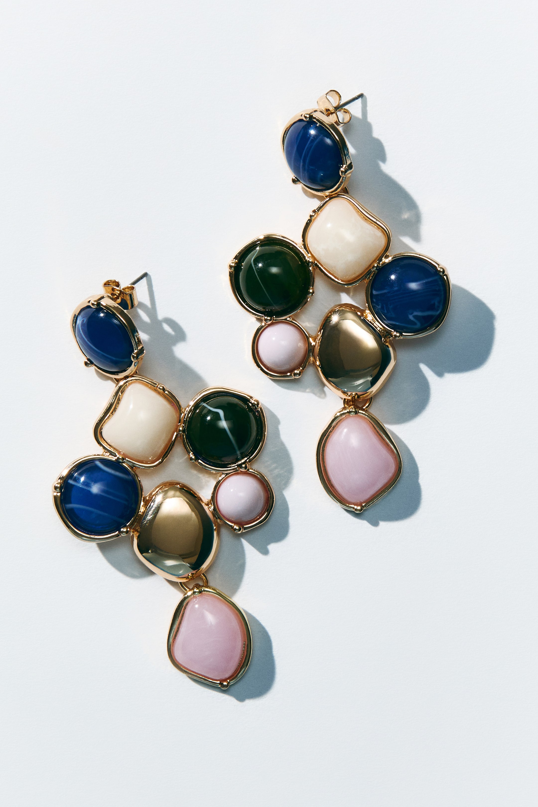 Agrandir l'image: Boucles d'oreilles pendantes en métal ornées de perles en plastique aux motifs variés, mettant en valeur leur face avant. Les montures en métal doré relient un assortiment de perles en plastique, qui se présentent sous des formes rondes, organiques et carrées rembourrées, et sont colorées en bleu, vert foncé, crème, rose clair et or métallique.