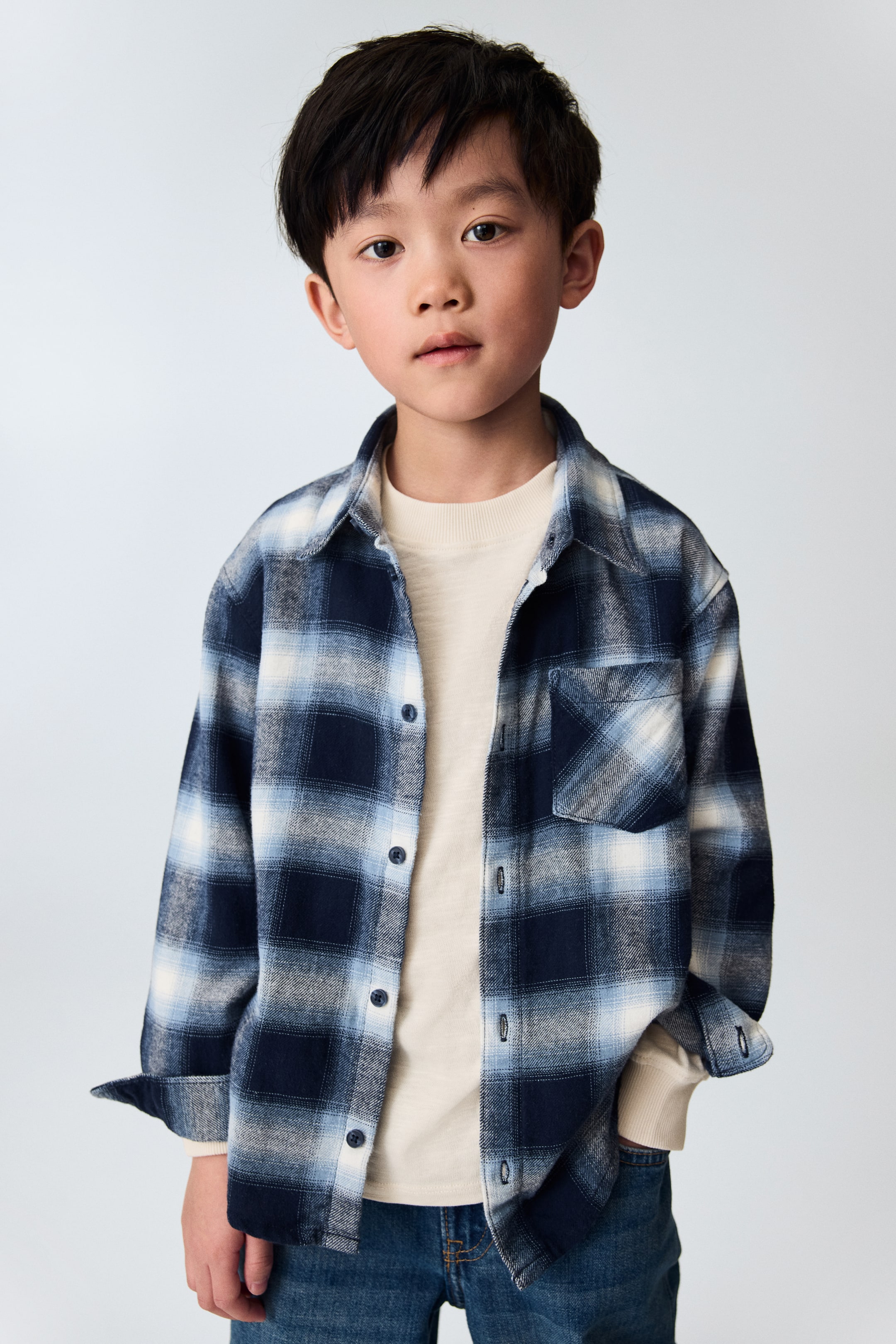 View larger image: A blue, light blue, and white check button-down shirt is facing forward, featuring a standard collar, a button-down front, and one chest patch pocket. Its long sleeves are rolled up, revealing a light-coloured undershirt.