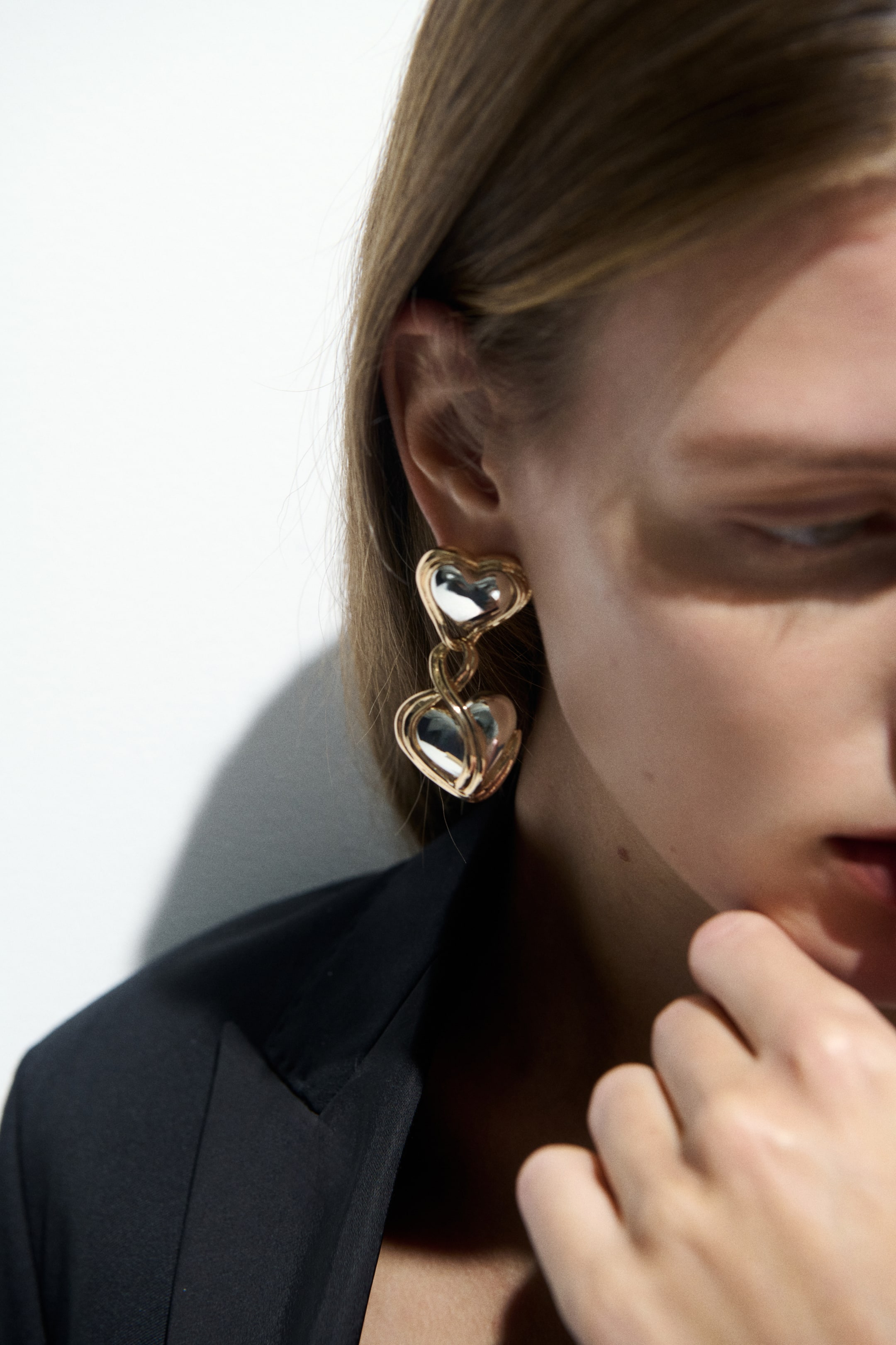 View larger image: A two-tone drop earring, featuring two heart-shaped components with reflective silver-toned centers and gold-toned wire outlines, is worn on the model's ear.