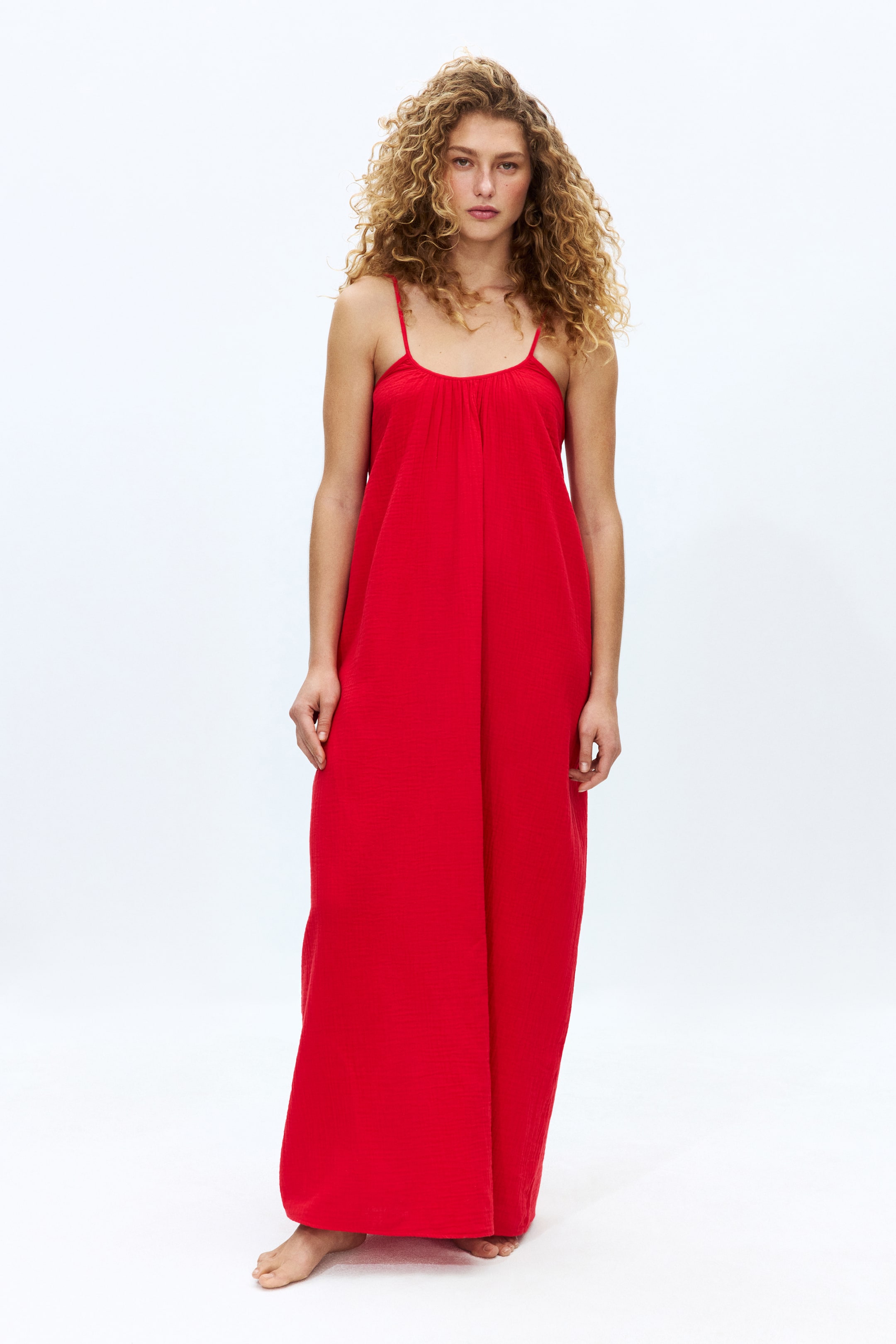View larger image: A red maxi dress featuring thin spaghetti straps and a gathered scoop neckline, with its flowing, textured fabric extending to the ankles.
