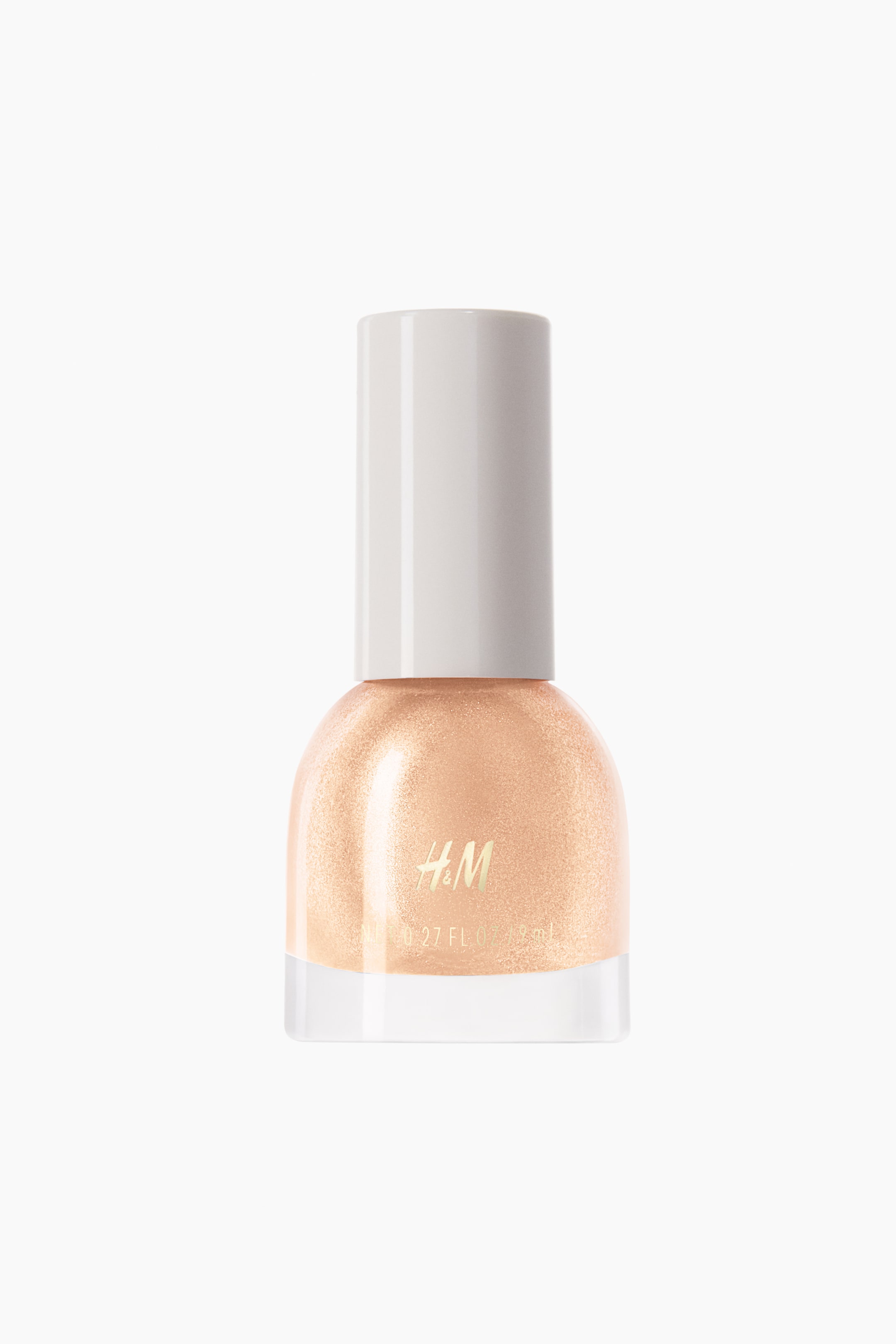 View larger image: The nail polish bottle is positioned upright, showcasing a transparent glass base filled with a light peach, shimmery polish. It is crowned with a white cylindrical cap, and the H&M logo along with '0.27 FL OZ / 8 ml' text is prominently displayed in gold on the front of the bottle.