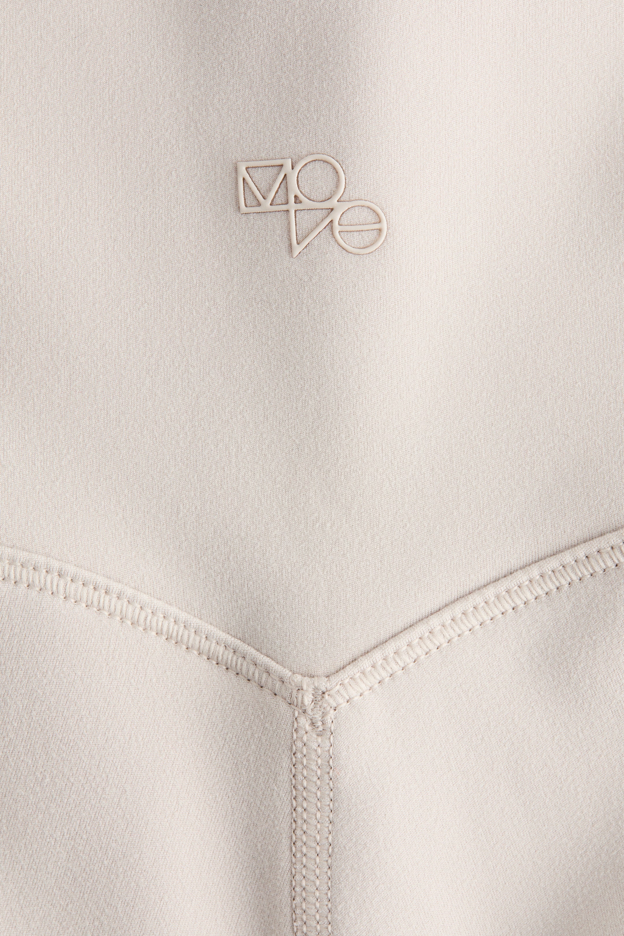 Visualizza immagine più grande: I pantaloncini da ciclismo sportivi con SoftMove presentano un tessuto beige chiaro con una trama sottile. Un logo stilizzato e geometrico 'MOVE' è in rilievo sulla parte superiore sinistra, e una cucitura flatlock prominente a forma di V dettaglia la sezione inferiore.