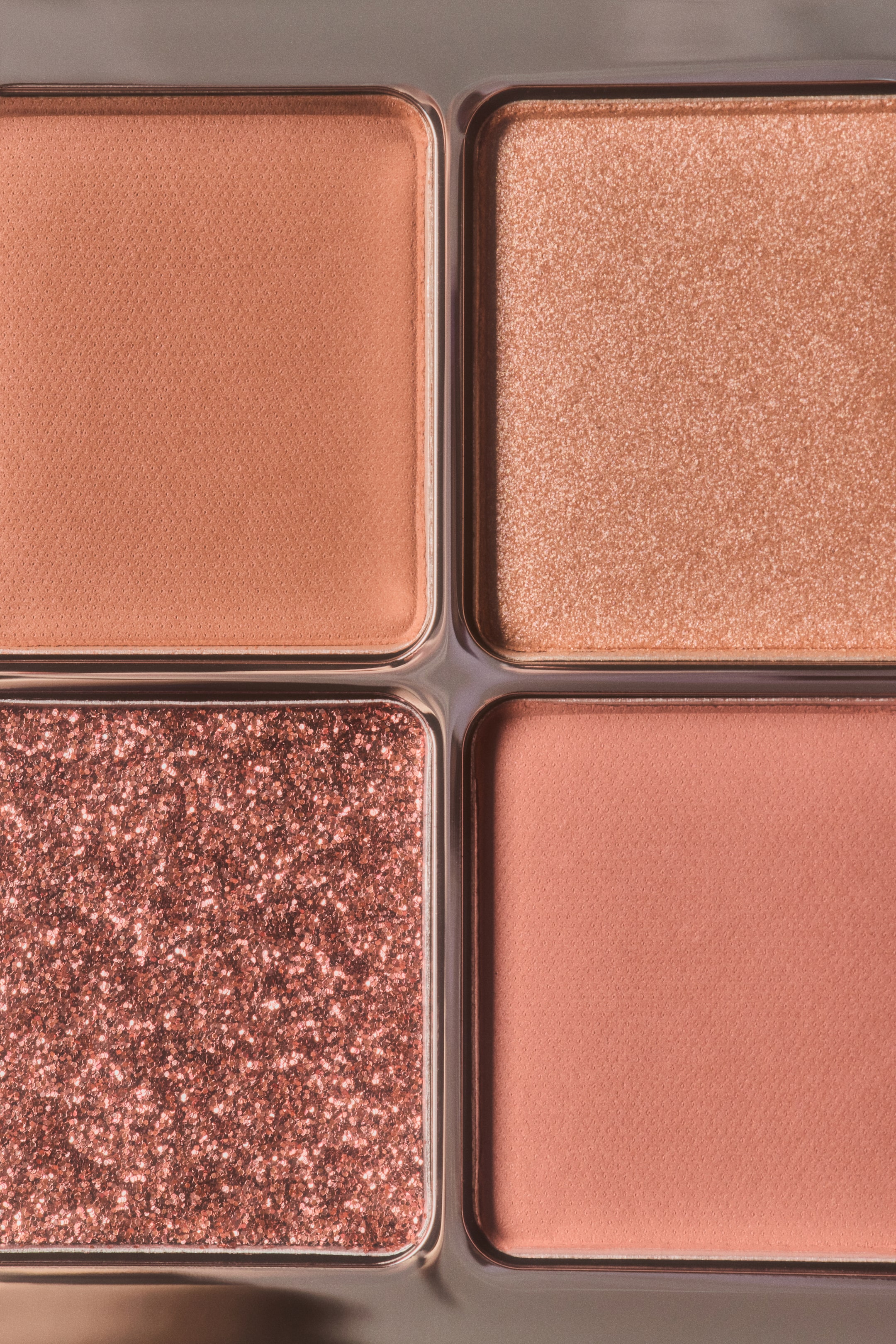 Grösseres Bild ansehen: Eine Nahaufnahme einer Lidschatten-Quad-Palette mit vier warmen, pfirsich- und roséfarbenen Nuancen in einem 2x2-Raster. Die Palette umfasst zwei geschmeidige matte Farbfächer in Pfirsich und staubigem Rosa, ein feines Champagner-Schimmer-Fach sowie ein strukturiertes, glitzerndes Rose-Gold-Fach.