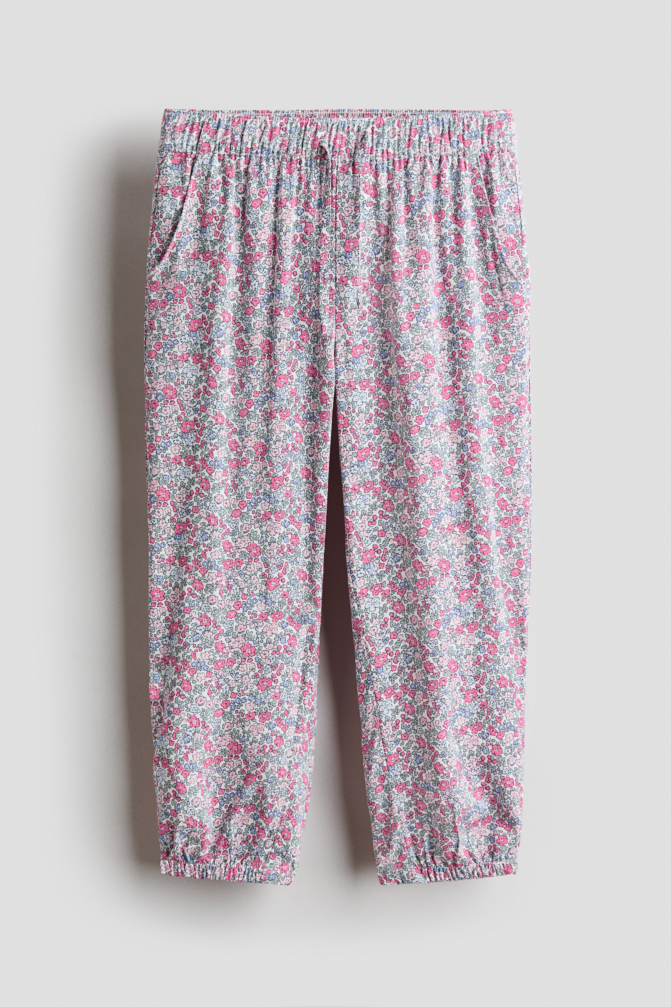 Größeres Bild anzeigen: Jogginghosen werden von vorne präsentiert und bestehen aus einem weichen Viskosegewebe mit einem kleinen Blumenmuster in Rosa, Blau und Weiß. Sie sind mit einem überzogenen, elastischen Bund gestaltet, der eine dekorative Schleife als Kordelzug vorne hat, Seitentaschen und elastische Bündchen.