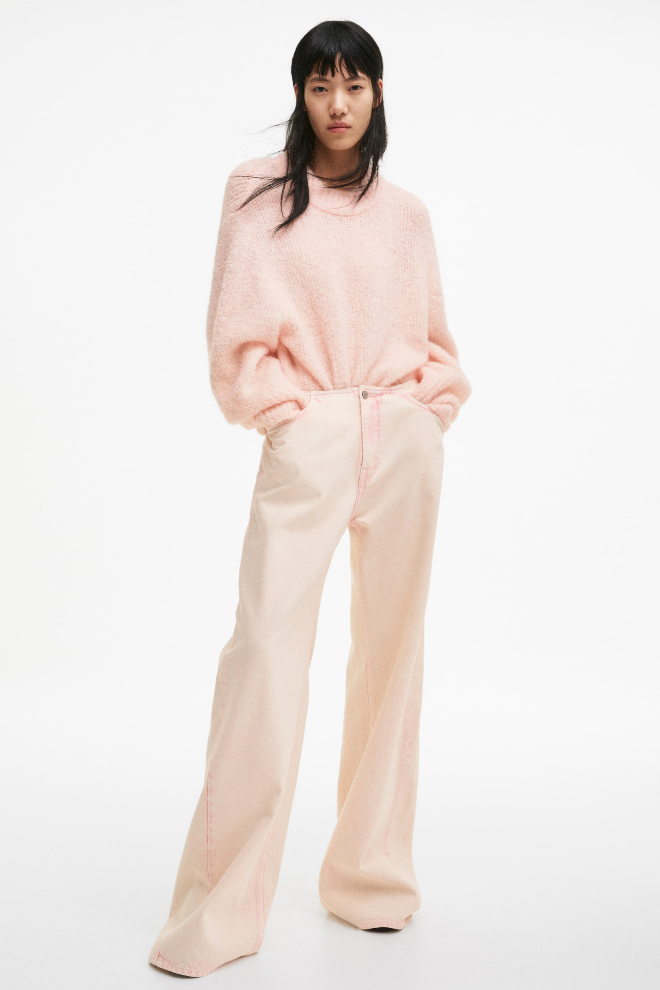 View larger image: A pink brushed knit crew neck sweater is styled, partially tucked into high-waisted, wide-leg pale pink jeans with visible pink stitching. The sweater boasts voluminous sleeves.