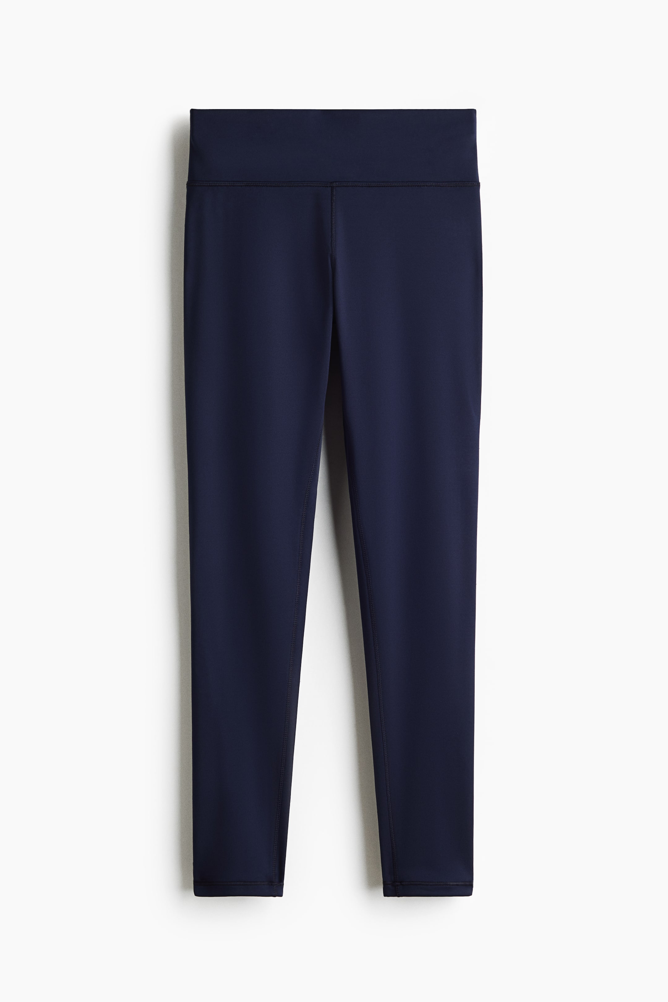 View larger image: These navy blue leggings are shown from the front, featuring a wide, high-rise waistband and flatlock seam detailing along the centre and inner legs. The fitted, ankle-length style showcases a minimalist design with tonal stitching.