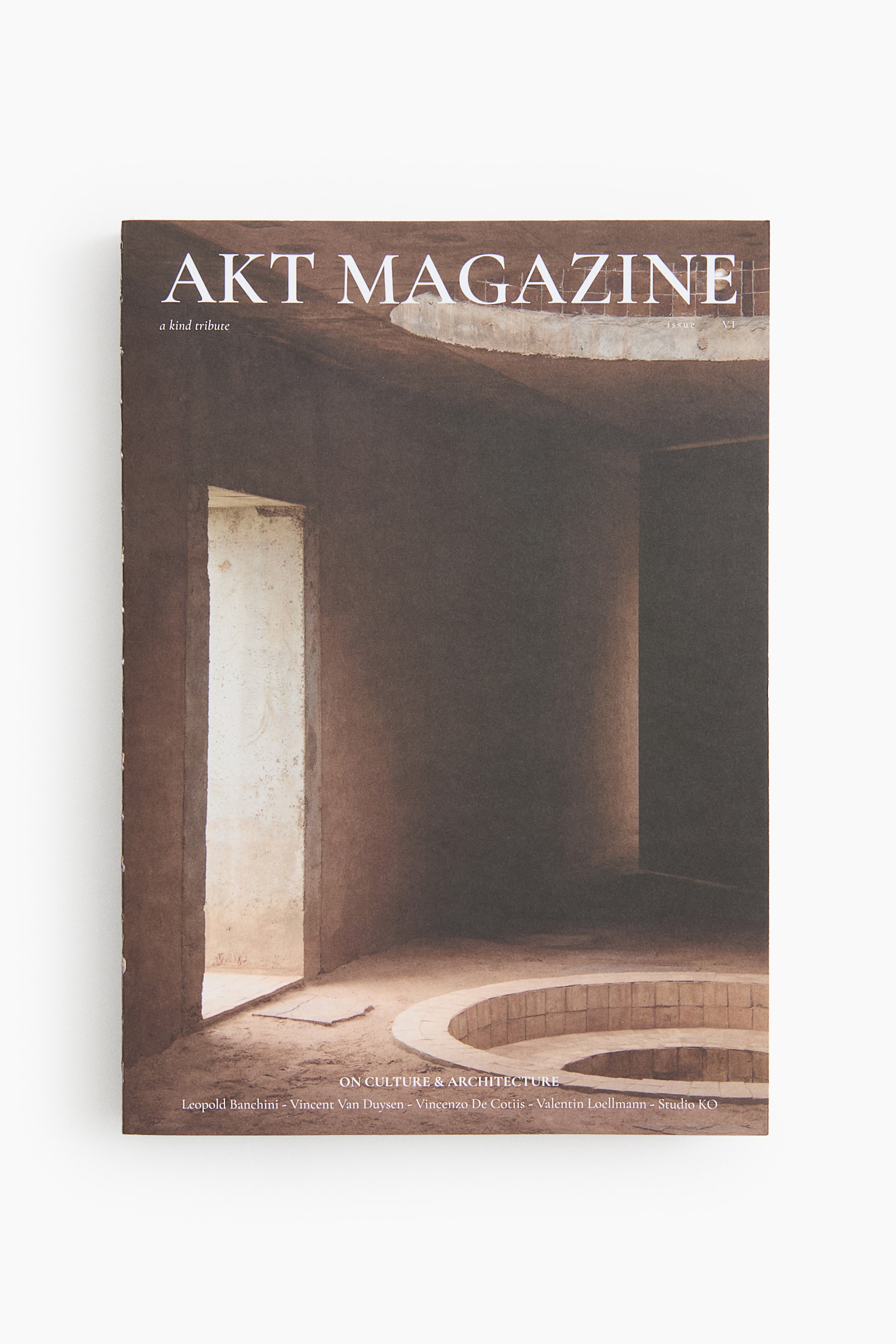 Visa större bild: Produkten är ett nummer av Akt Magazine och visar omslaget på framsidan, där ett fotografi av en minimalistisk arkitektonisk interiör i varma bruna och beige toner med en öppen dörröppning och en cirkelformad inbyggd detalj framträder. På omslaget står ”AKT MAGAZINE” högst upp, ”a kind tribute” under det samt ”ON CULTURE & ARCHITECTURE” tillsammans med en namnlista längst ned.