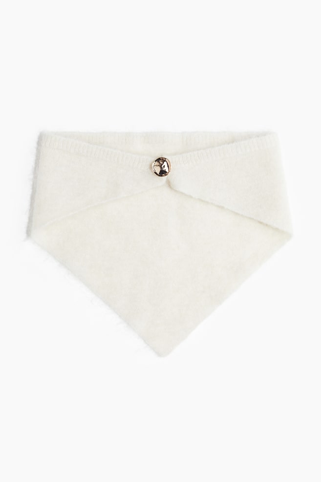 A cream-colored soft knit neck warmer is featuring a folded top edge, secured by a single, round, hammered gold-toned button. The warmer is shaping into a point at its bottom. - 1