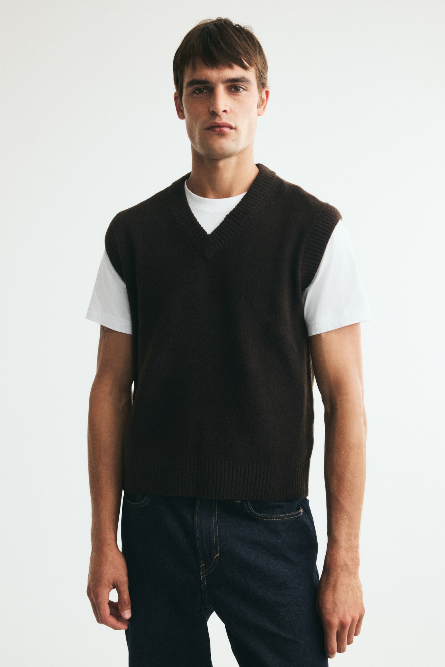 A dark brown sweater vest is featuring a V-neckline with ribbed trim, ribbed armholes, and a ribbed hem. It is displaying a softly textured knit fabric from the front. - 1