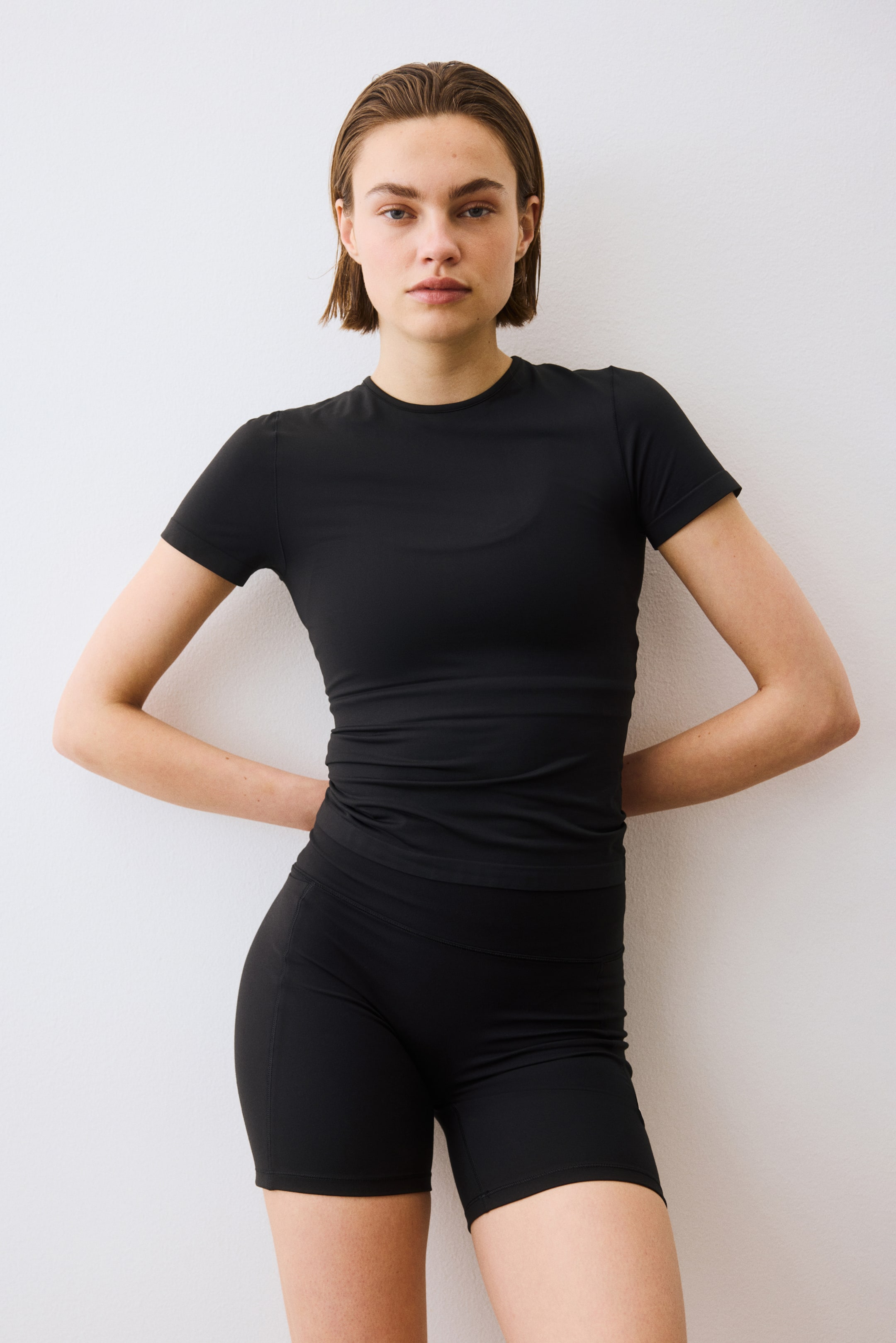 View larger image: A black short-sleeved crew neck top showcases a snug fit. Black mid-thigh length athletic shorts with a broad waistband also offer a snug fit.