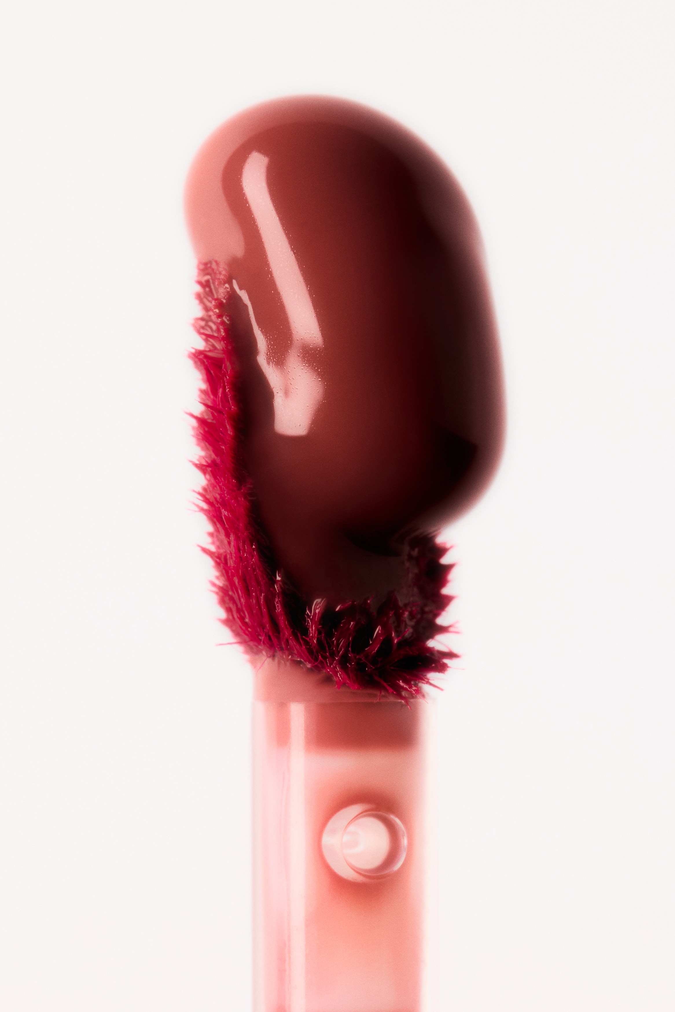 Um frasco de tinta labial rosa estÃ¡ na vertical e virado para a frente, apresentando um recipiente retangular em vidro fosco transparente que revela um reservatÃ³rio rosa central no interior. O recipiente Ã© rematado por uma tampa cilÃ­ndrica metÃ¡lica prateada e exibe texto branco vertical na frente com a inscriÃ§Ã£o "GLOSS TINT" e "Glossy Lip Tint".