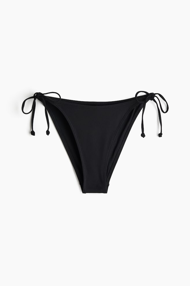 Czarne majtki bikini prezentują widok z przodu, charakteryzują się w pełni podszytym projektem, średnim, zaokrąglonym stanem, wiązaniami po bokach oraz wyciętym krojem z tyłu. - 1
