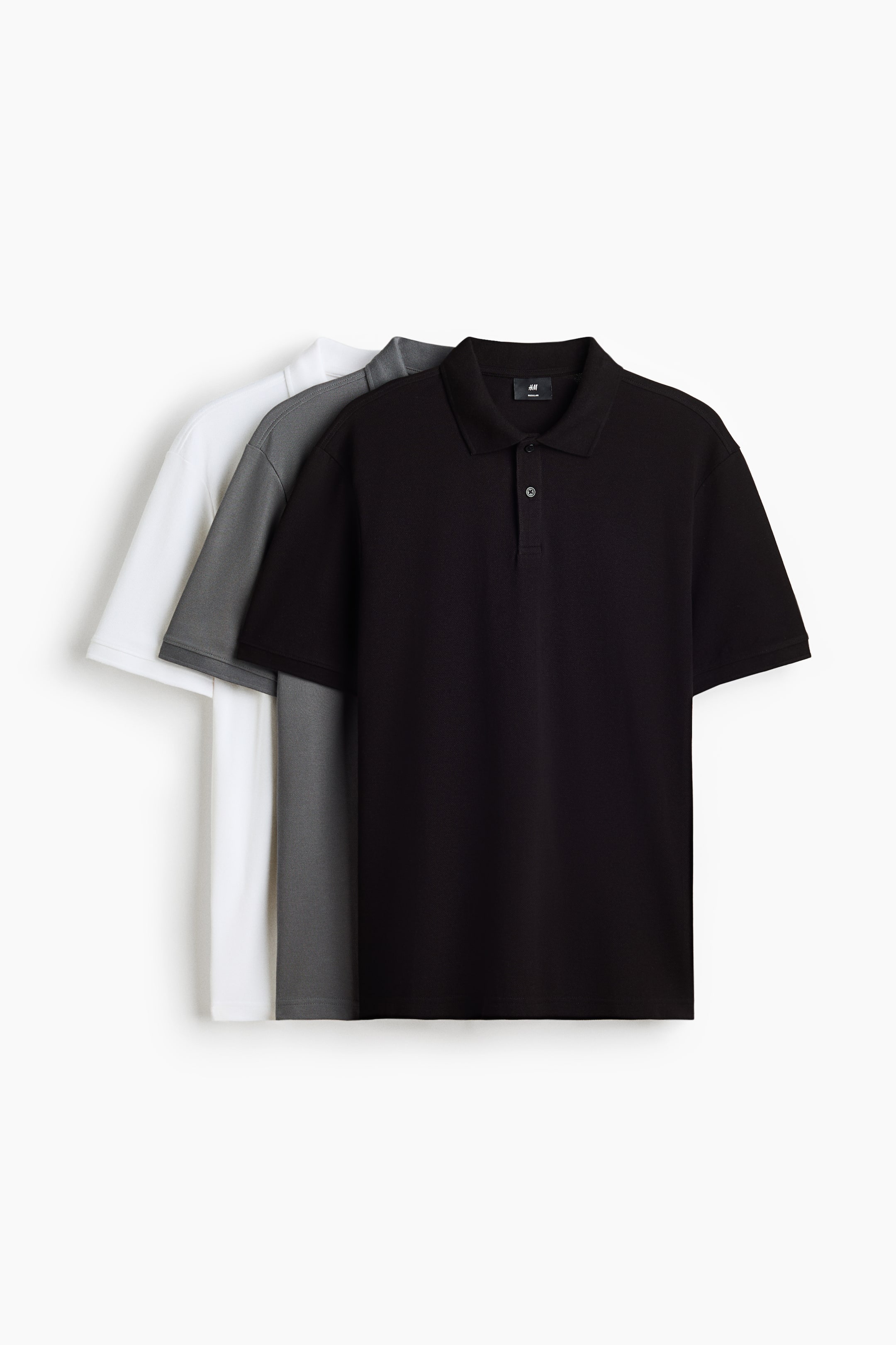 View larger image: A 3-pack of regular fit polo shirts is layered, presented in black, dark grey, and white. Each polo features a classic collar, a two-button placket, and short sleeves, all facing front.