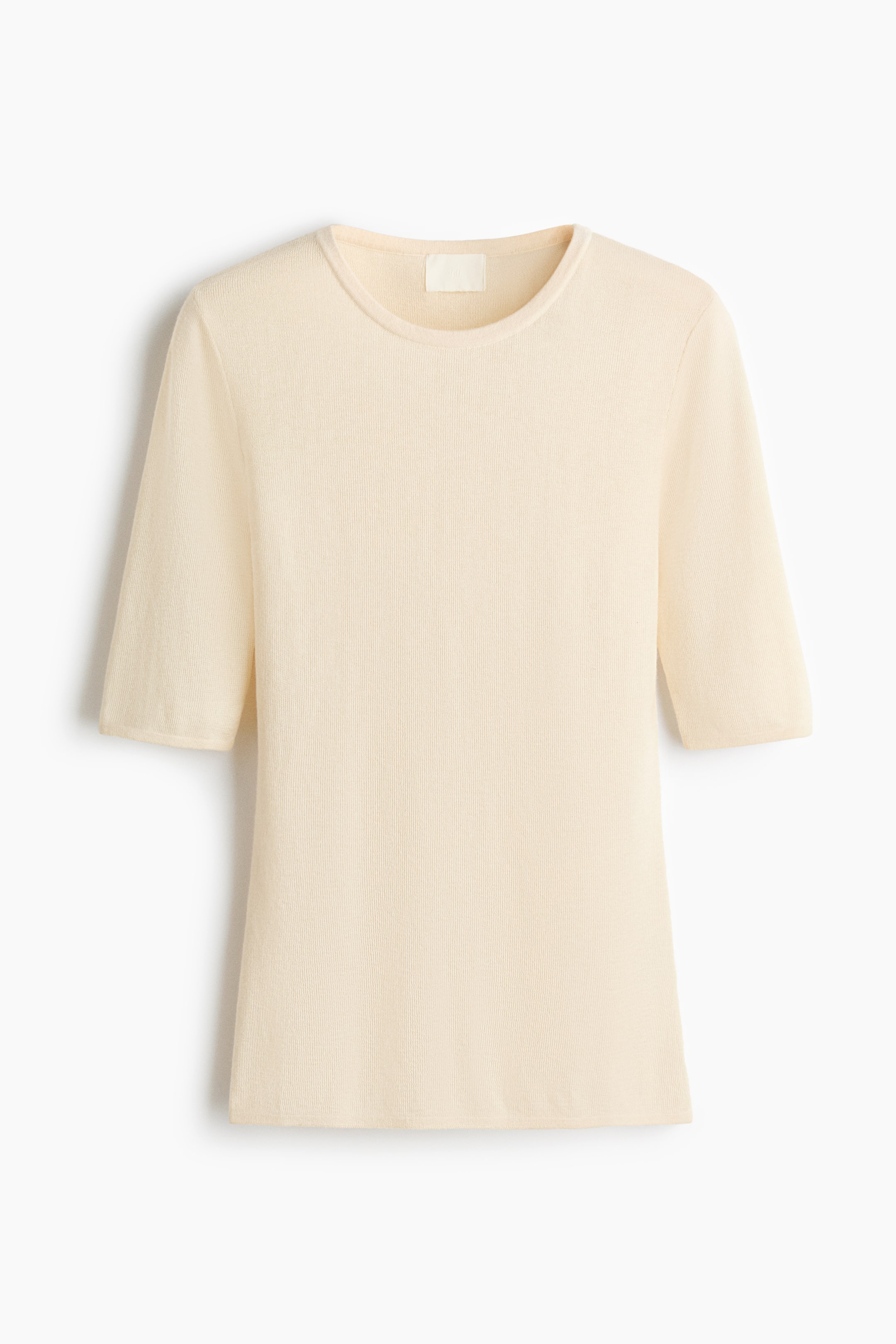 View larger image: A cream-colored, fine-knit top is presenting front, featuring a crew neck and elbow-length sleeves. A subtle vertical ribbed texture is visible throughout the garment, and a small label is showing at the inner back neck.