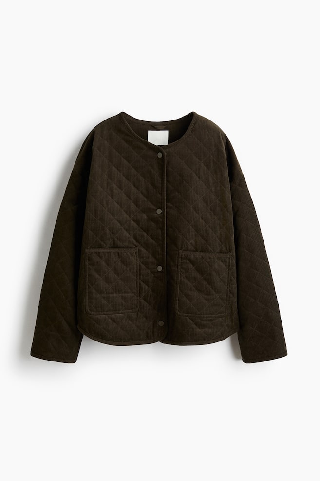 Se presenta una chaqueta de pana acolchada de color marrón oscuro, sin cuello, desde el frente, con un patrón de acolchado en forma de diamante, cierre frontal con botones a presión y dos bolsillos de parche inferiores. - 1
