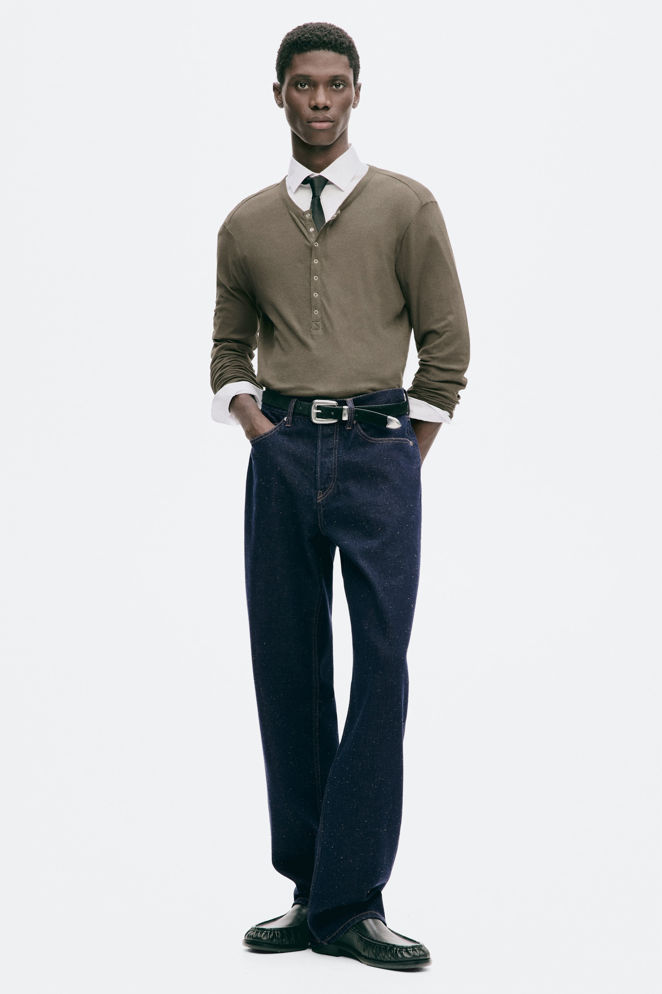 Grösseres Bild ansehen: Dunkelblaue Denim-Jeans mit geradem Bein in regulärer Passform werden vom Model getragen und mit einem schwarzen Ledergürtel in der Taille gestylt. Das Model steht mit einer Hand in der vorderen Tasche und zeigt den lockeren Fall sowie den geraden Schnitt der Beine.