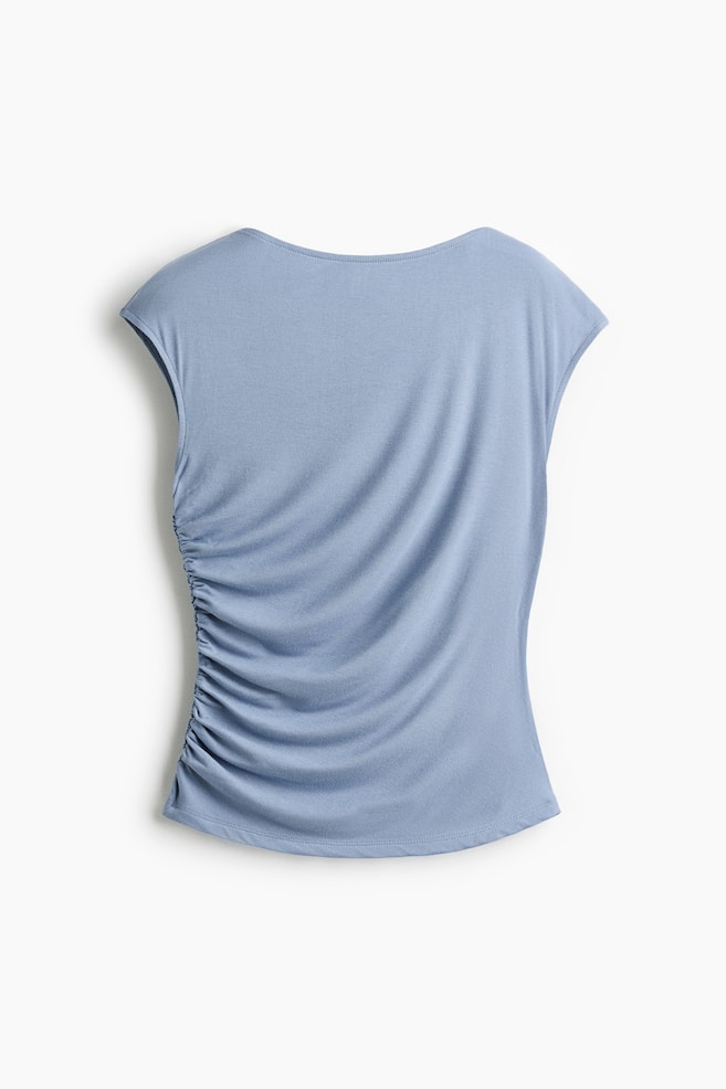 A light blue top is displaying its back view, featuring a wide boat neckline and cap sleeves. The left side of the torso is gathered with vertical ruching, while the right side remains smooth, and the hem is gently curved. - 1