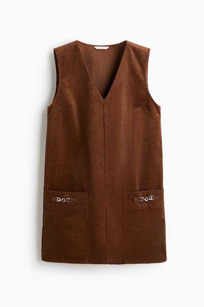 Un vestido corto sin mangas de pana de algodón suave se presenta en el frente. Presenta una silueta en línea A con un escote en V, bolsillos grandes detallados con eslabones de cadena de metal y un dobladillo de corte recto. - 1