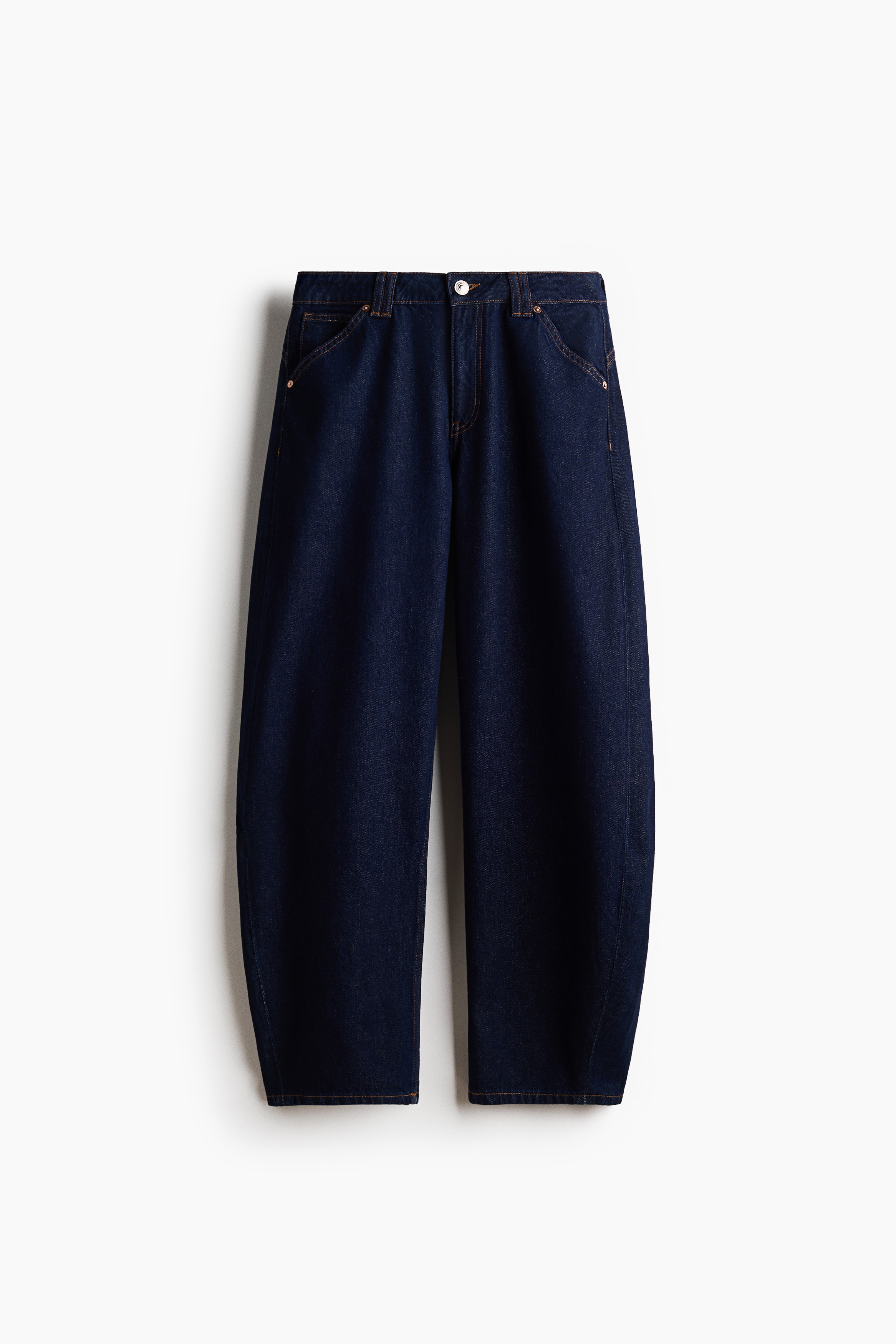 These dark blue, five-pocket denim jeans showcase a loose, curved silhouette that tapers toward the hems as the wearer stands on a skateboard angled to the right. The sturdy jeans are styled with a layered striped T-shirt and white sneakers, highlighting their regular length and relaxed fit.