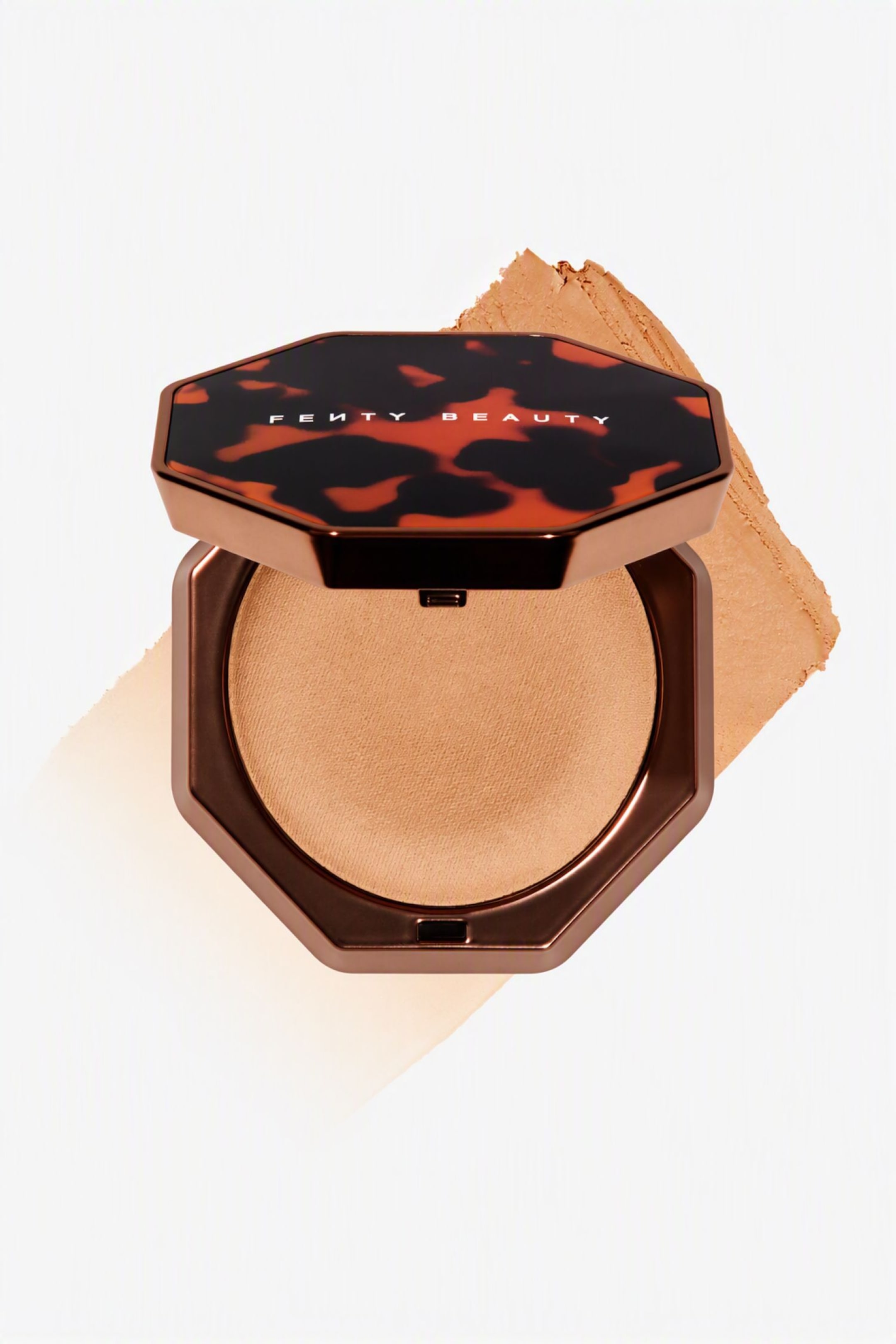Visa större bild: En öppen, åttkantig kompakt visar en ljusbrun pressad bronzer, placerad ovanpå ett diagonalt, texturerat drag av samma nyans. Kompakten har en metallisk bronsfärgad bas och ett sköldpaddsmönstrat lock med "FENTY BEAUTY" tryckt i vita bokstäver.
