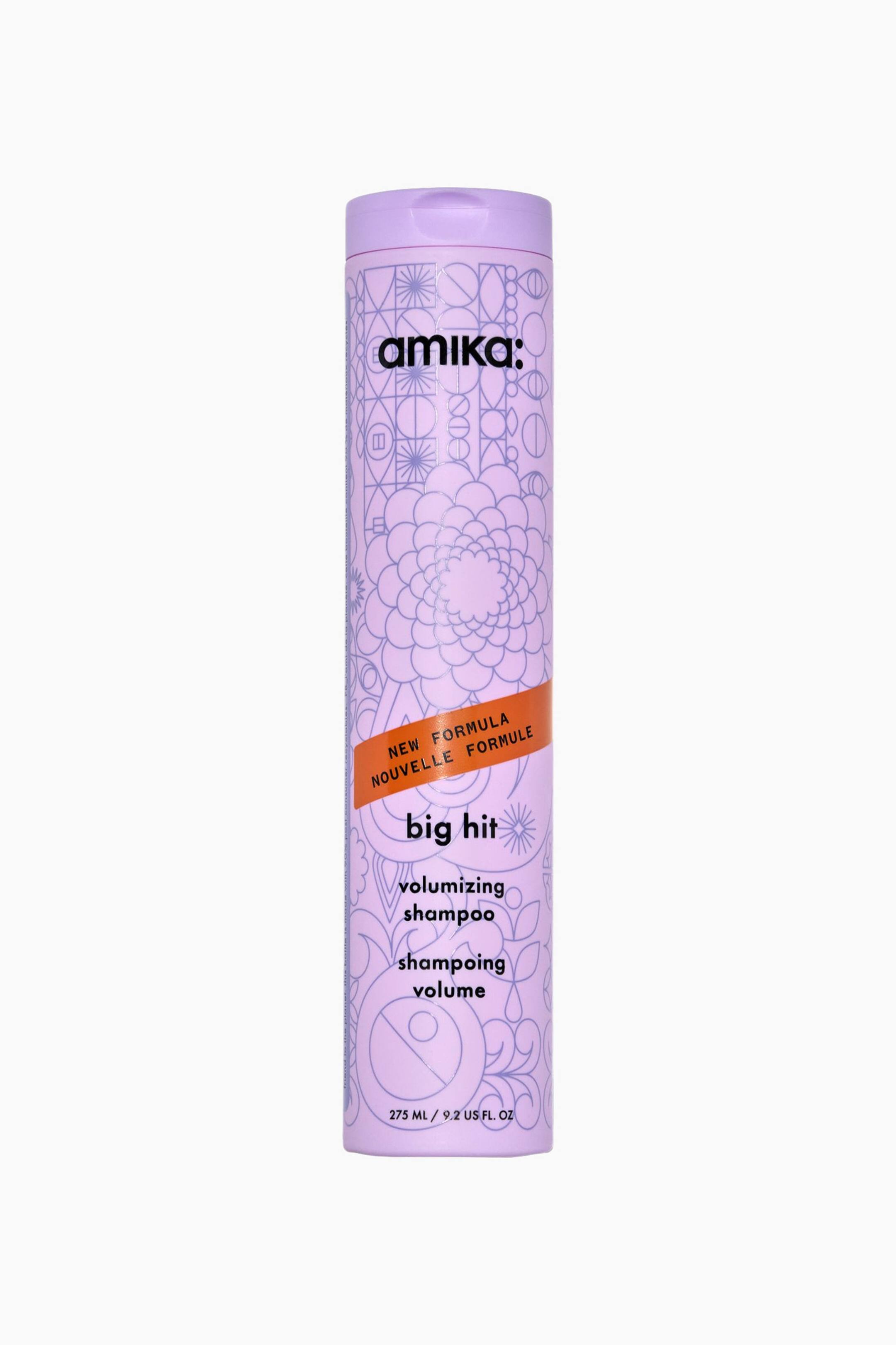 Visa större bild: En hög, cylindrisk lavendelfärgad flaska med amika Big Hit Volumizing Shampoo står upprätt i en frontvänd vy. Flaskan har intrikata lila linjetecknade mönster av blommor och geometriska former, accentuerade av ett diagonalt orange band över mitten. Svart text på framsidan visar varumärket "amika:", produktnamnet "big hit volumizing shampoo" och volymen "275 ML / 9.2 US FL. OZ".