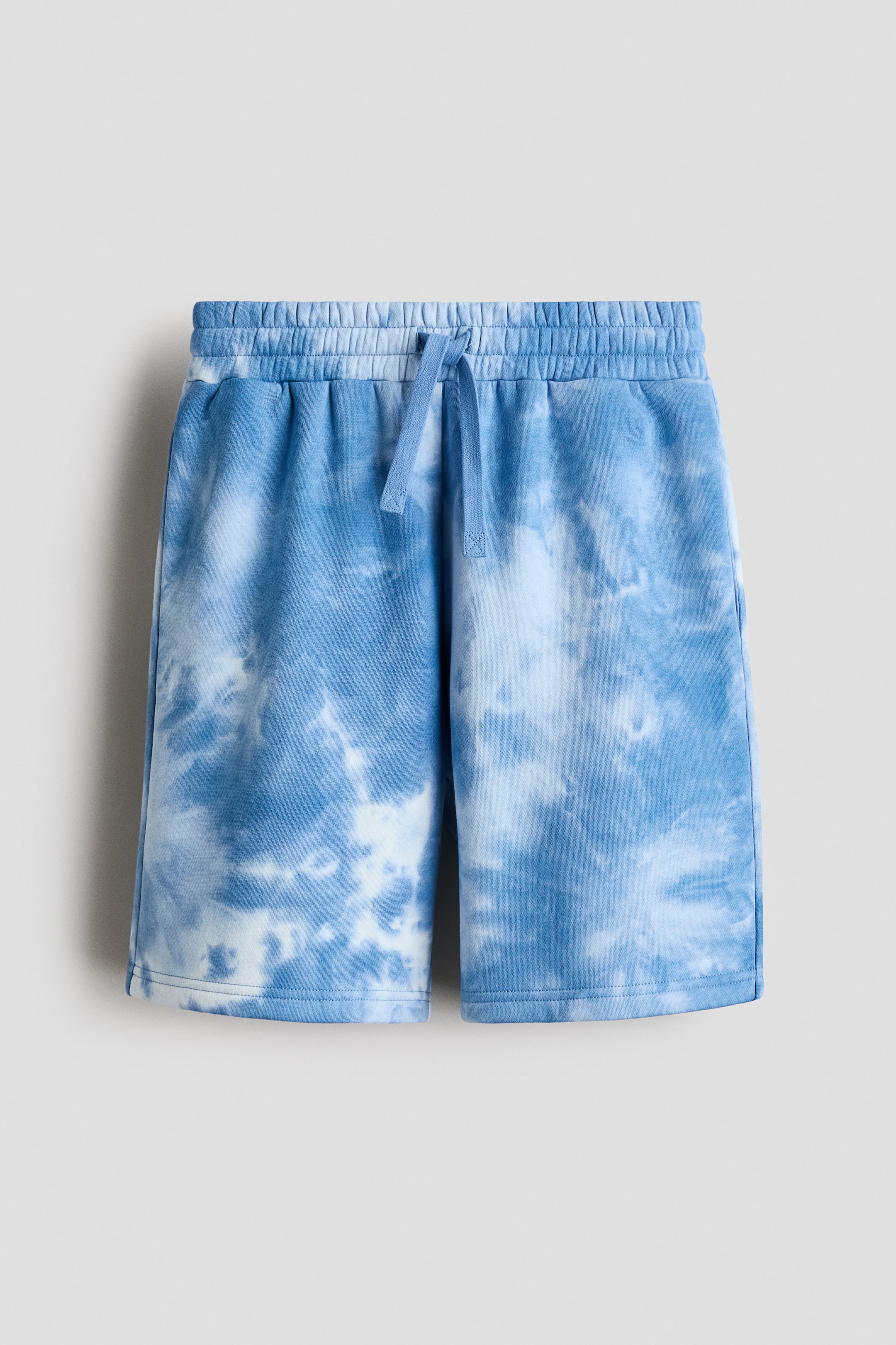 View larger image: Shorts exhibit a blue and white tie-dye pattern at the front, featuring an elasticated waistband with a blue drawstring and a stitched hem.