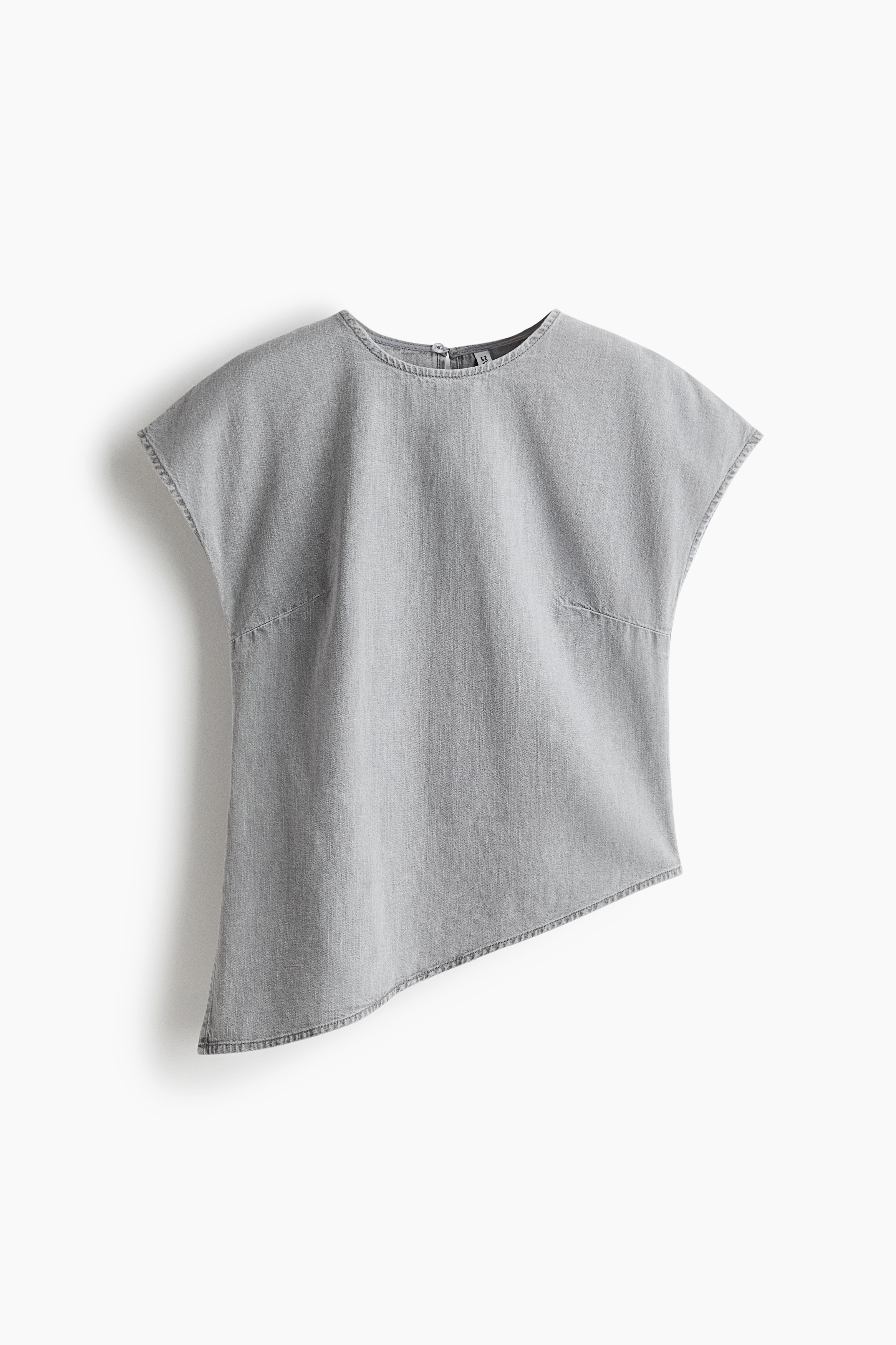 A light grey denim top with cap sleeves, a round neckline, and an asymmetric hem featuring a small side slit is worn by the model. The top is styled with black trousers.