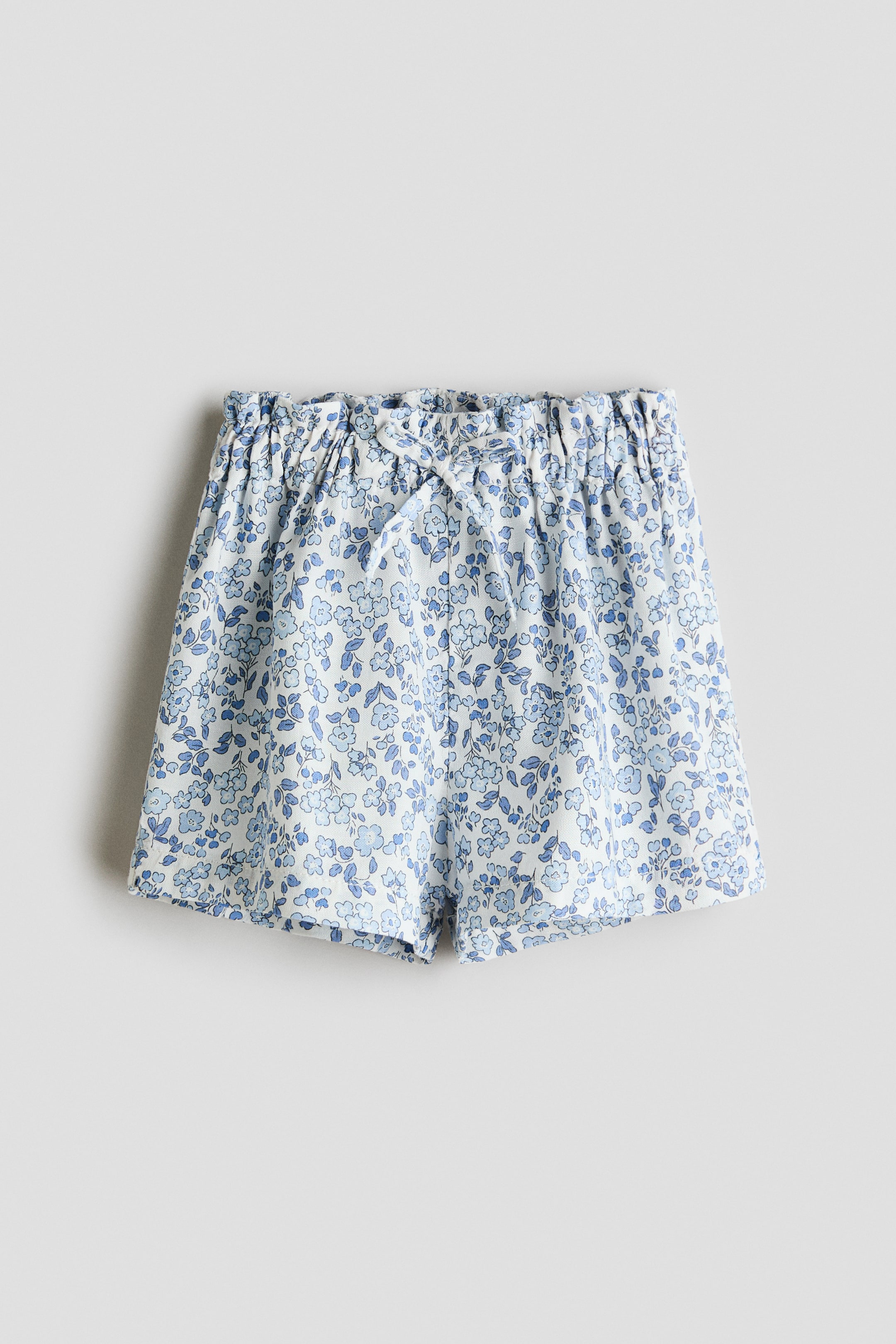 View larger image: These shorts feature a blue floral pattern on a light background, crafted from a soft weave, with an adjustable paperbag waist and a decorative bow tied at the front.