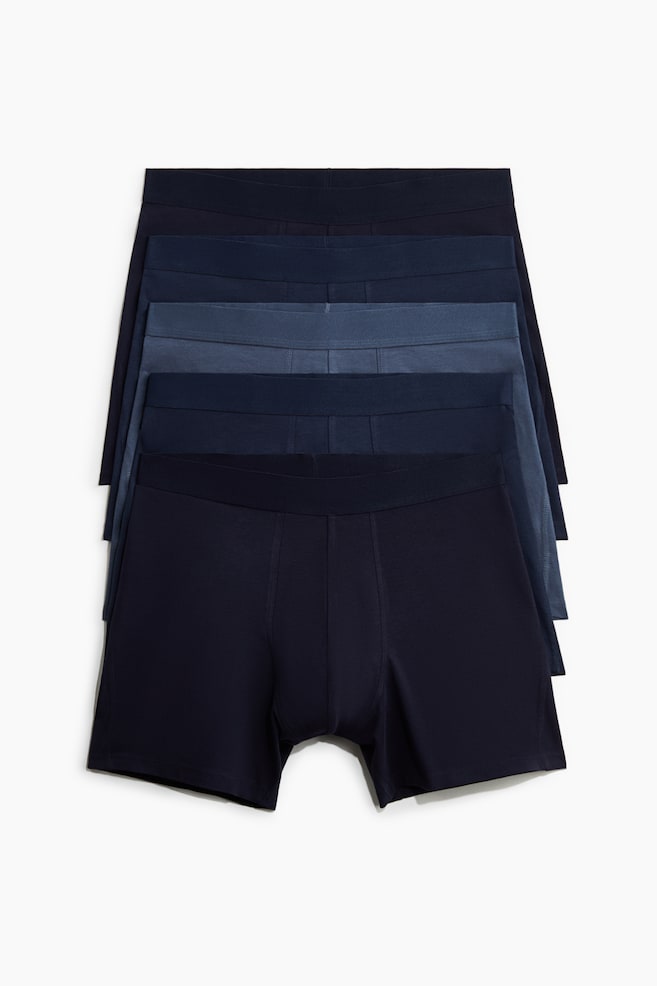 Fünf Paar Herren-Boxershorts sind gestapelt und zeigen einen Farbverlauf von Blautönen von dunkel bis hell. Die Vorderseite des unteren dunkelblauen Paares ist sichtbar und verfügt über einen elastischen Bund sowie ein konturiertes Frontpanel. - 1