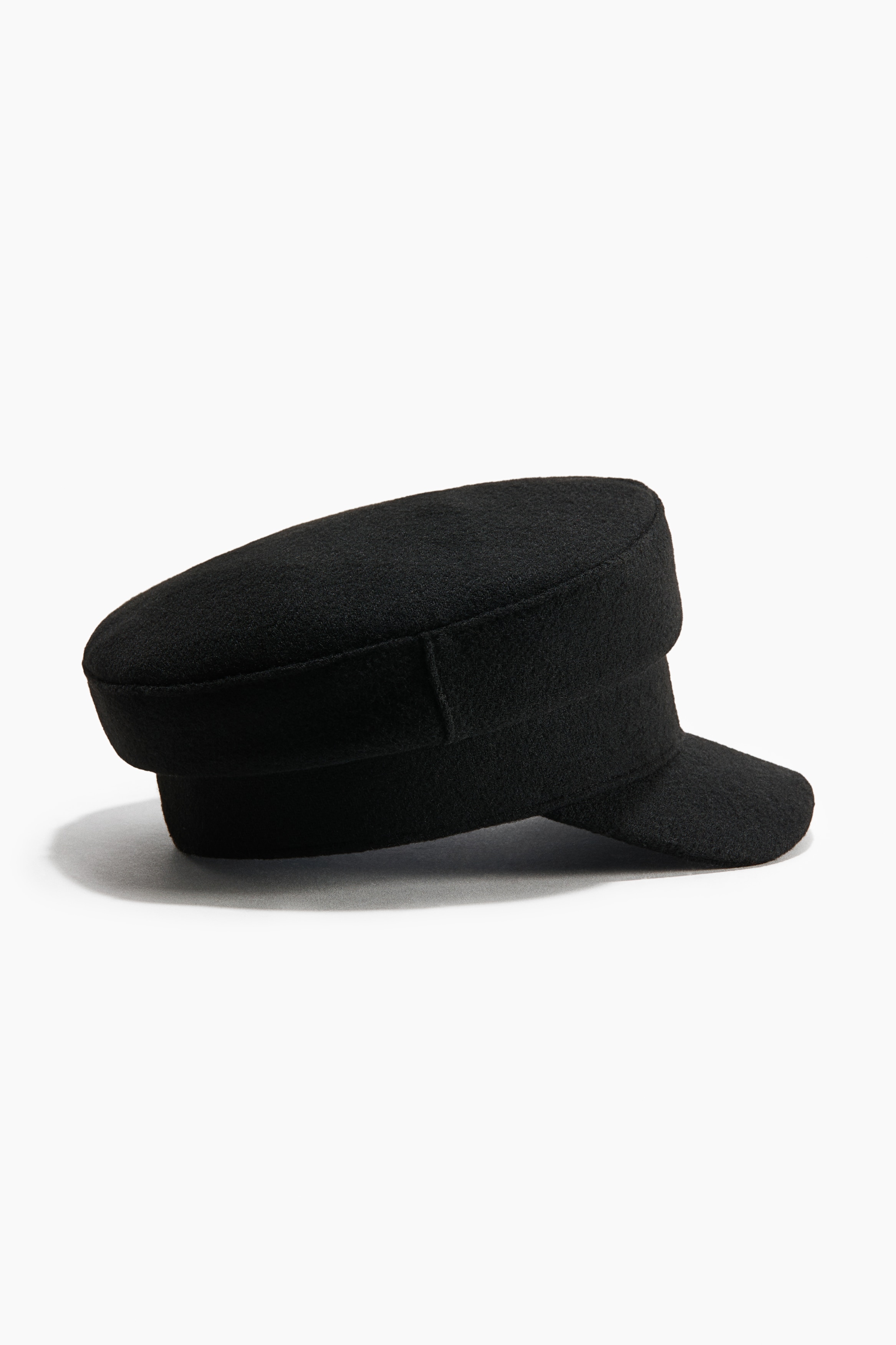 The model is wearing a black baker boy cap in woven fabric. The cap features a soft-structured, rounded crown with a short visor and is styled with a high-collared black knit top.