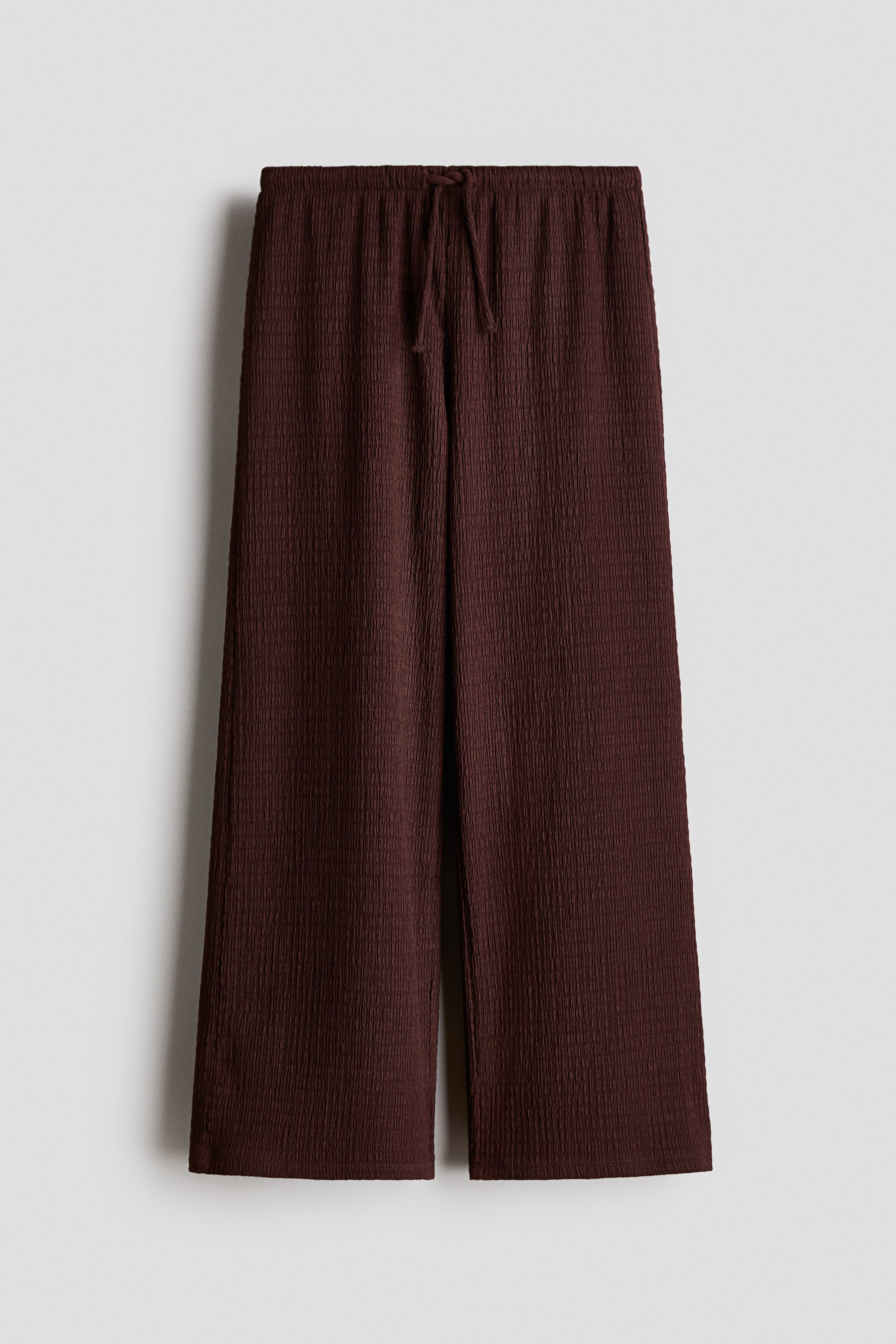 View larger image: The dark brown trousers showcase a textured jersey fabric, with an elasticated, drawstring waist and straight legs, all visible from the front.
