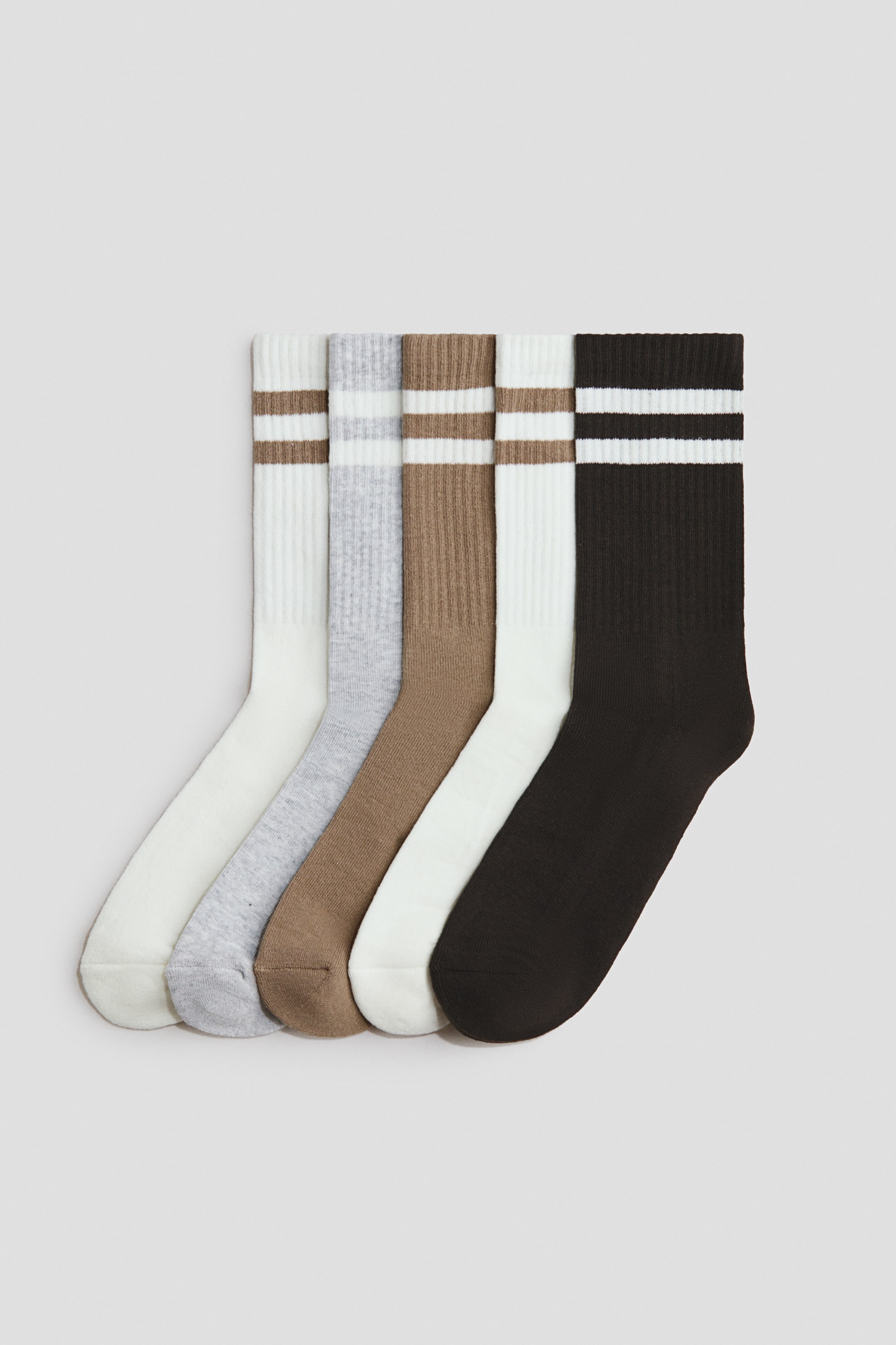 Größeres Bild ansehen: Fünf Paar Socken sind diagonal angeordnet und zeigen gerippte Schäfte und Bündchen. Die Socken umfassen ein cremefarbenes Paar mit braunen Streifen, ein hellgraues Paar mit weißen Streifen, ein braunes Paar mit weißen Streifen, ein weißes Paar mit braunen Streifen und ein dunkelbraunes Paar mit weißen Streifen, wobei jedes Paar zwei horizontale Streifen am Bündchen aufweist.