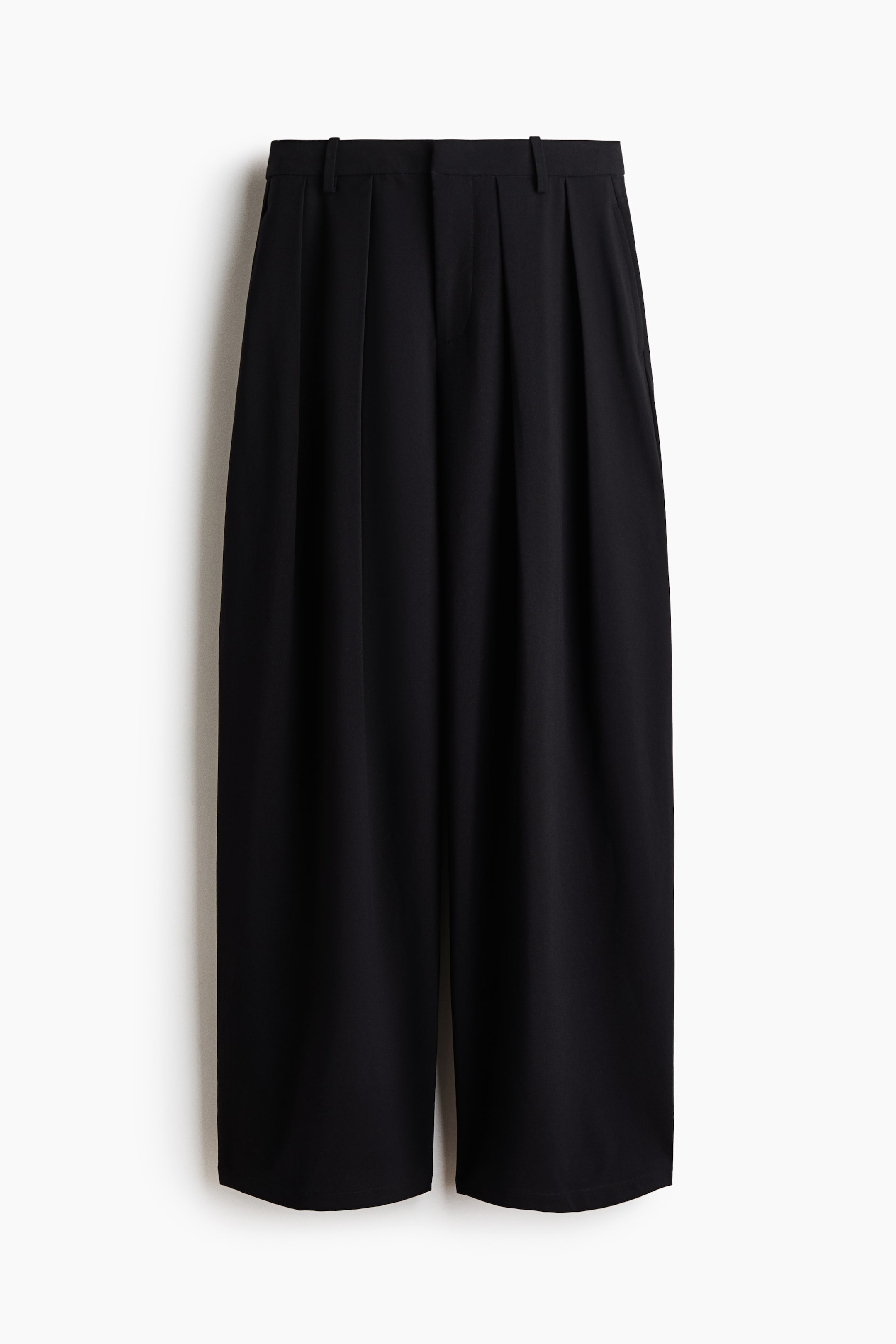 Größeres Bild anzeigen: Schwarze Hose, von vorne präsentiert, mit flachem Bund mit Gürtelschlaufen und markanten Bundfalten. Seitentaschen sind sichtbar, und die Hose zeigt eine weite, verkürzte Silhouette.