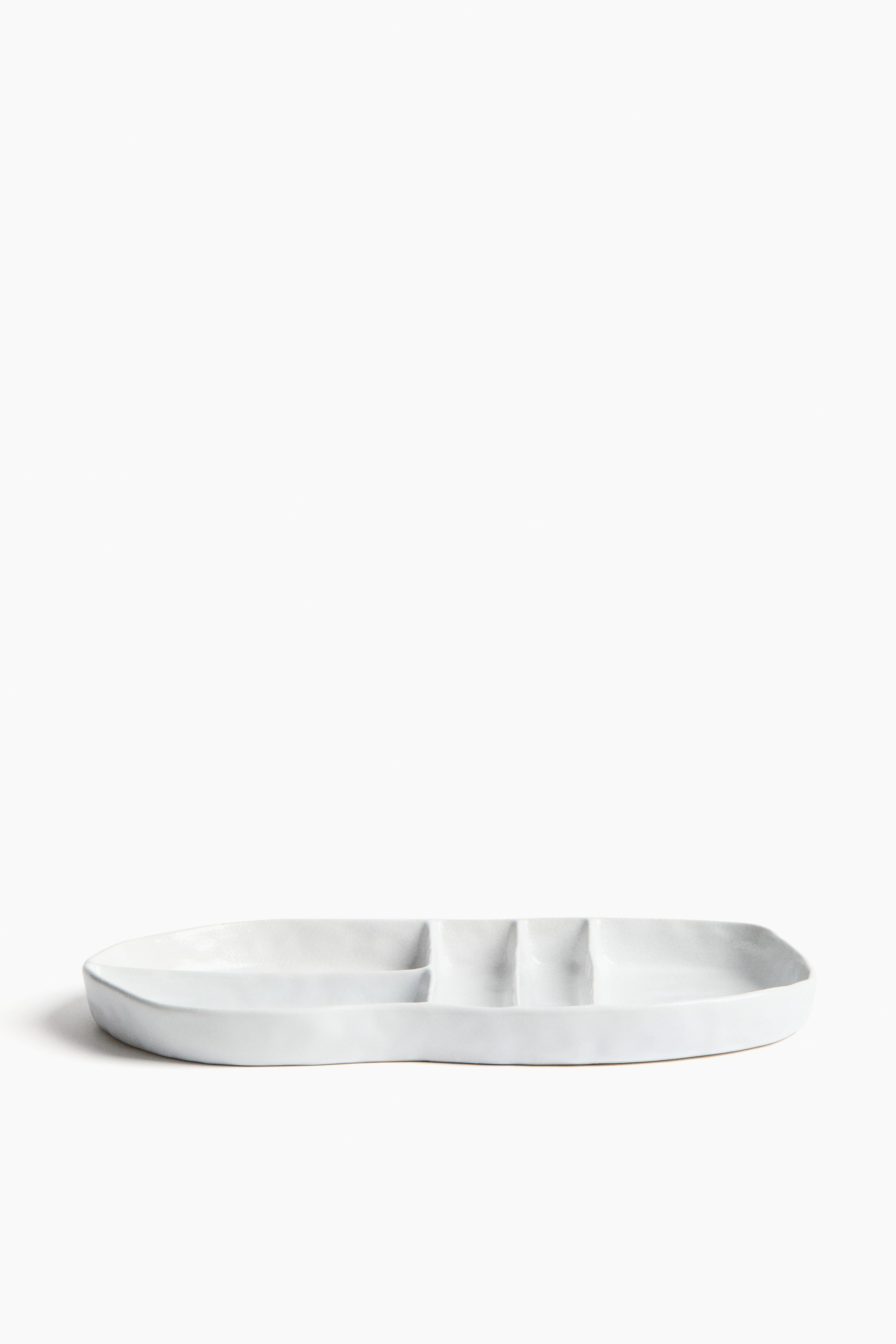 View larger image: A white ceramic serving dish presents an elongated, irregular oblong shape. It features three rectangular compartments running along its length, with subtly uneven edges.